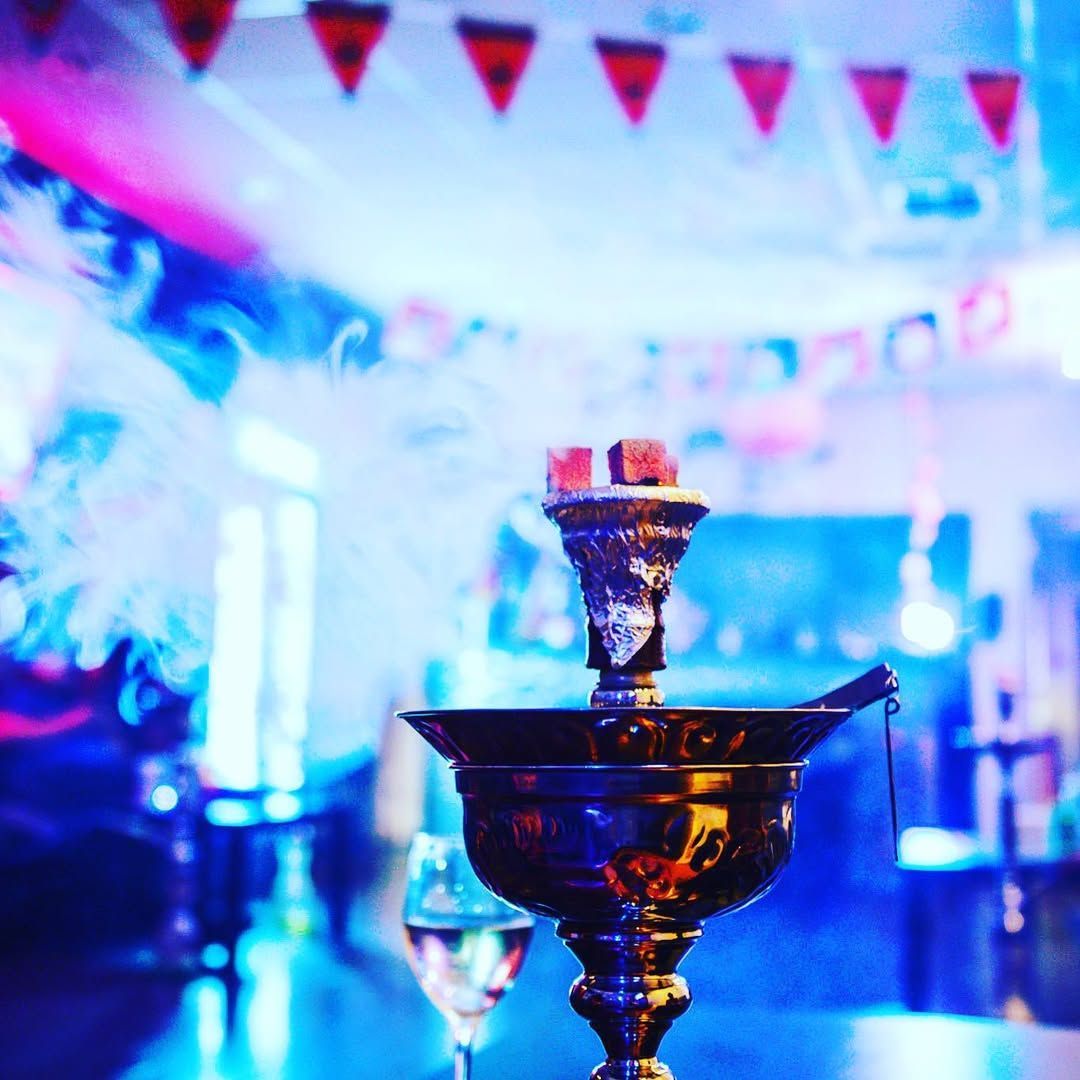 Hookah with lit coals, smoke rising in a dimly lit, festive room with blue and red lights.