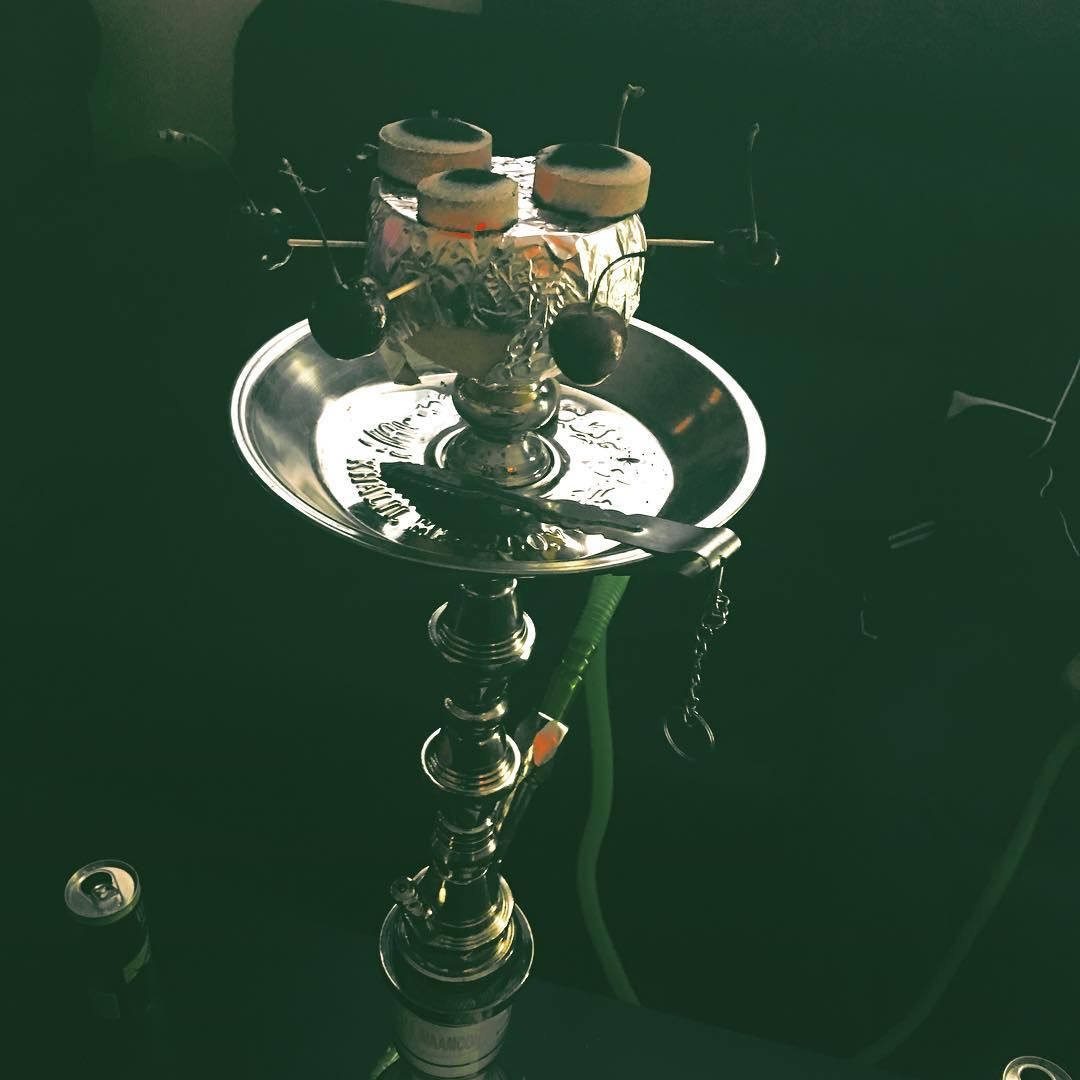 Hookah with lit coals, foil, and a green hose, on a black surface.