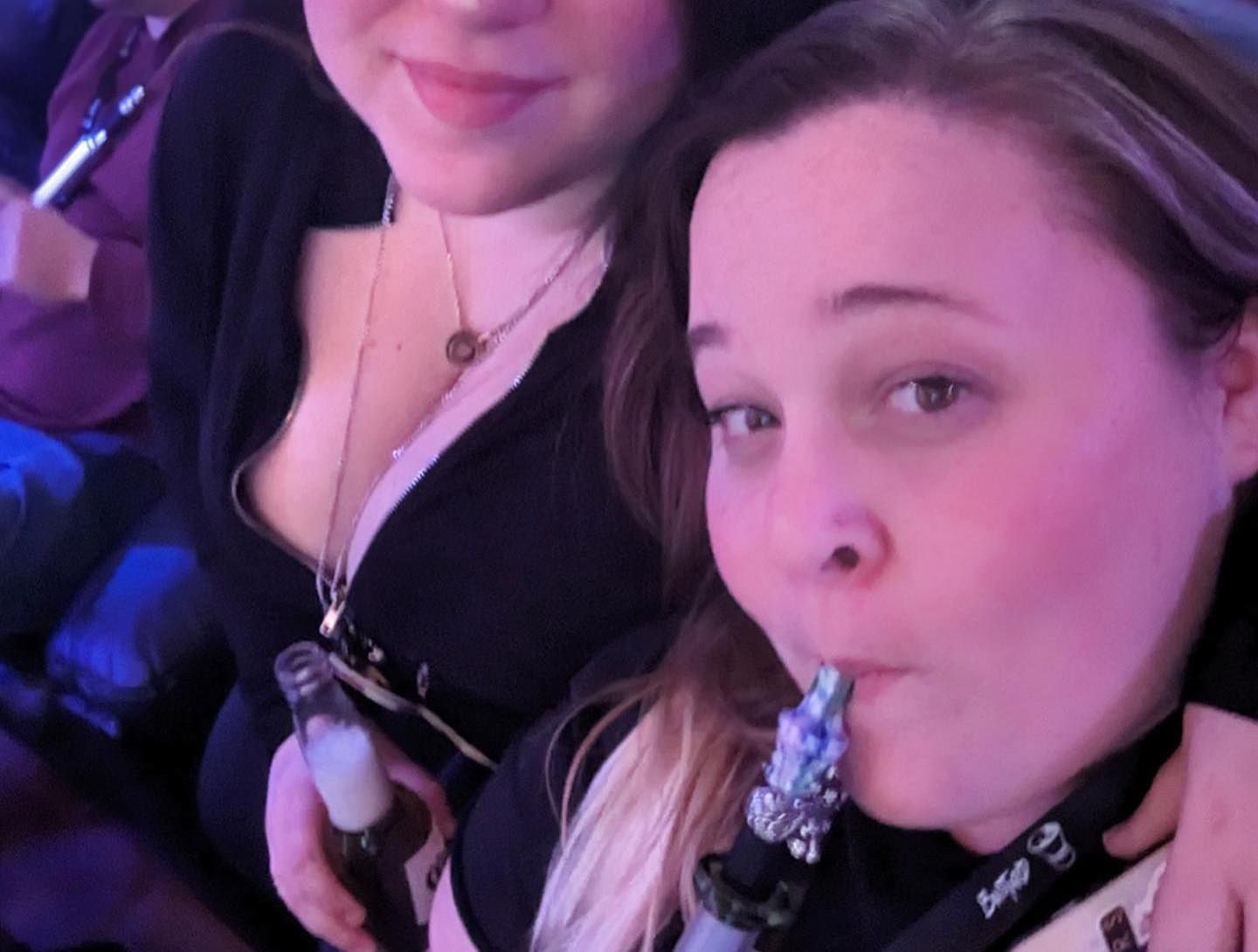 Two women, one smoking a hookah, the other holding a bottle. Both are smiling. Indoors, dim lighting.