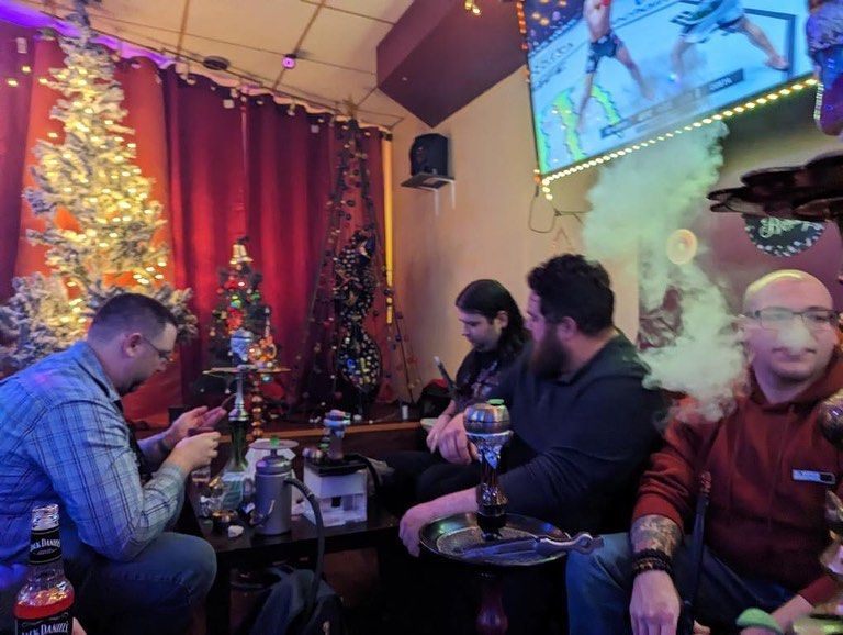 People in a hookah lounge with Christmas decorations, smoke, and a TV screen.