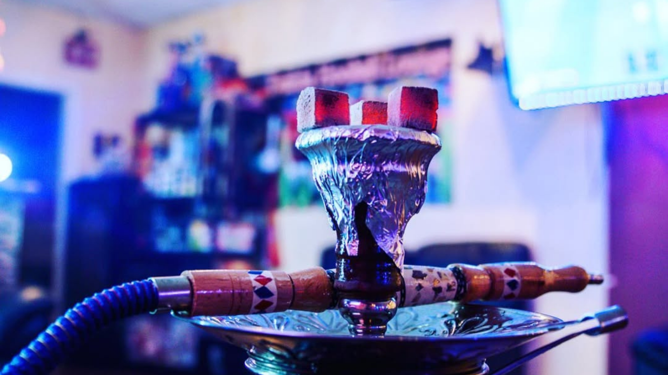 Hookah with lit charcoal on foil, blurry interior, blue and purple lighting.