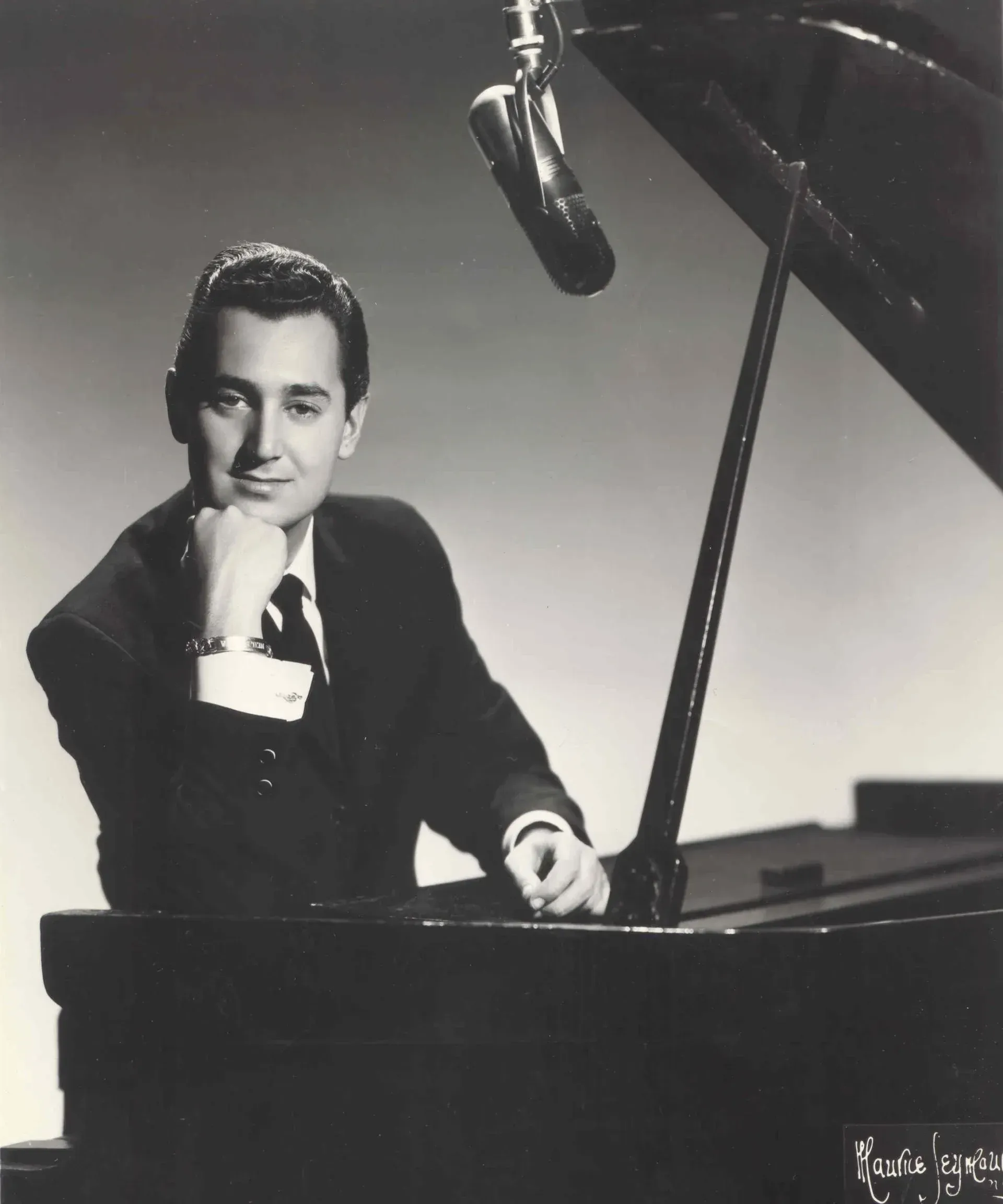 Sedaka im Anzug am Klavier, lächelnd, Hand am Kinn, Mikrofon über dem Kopf.