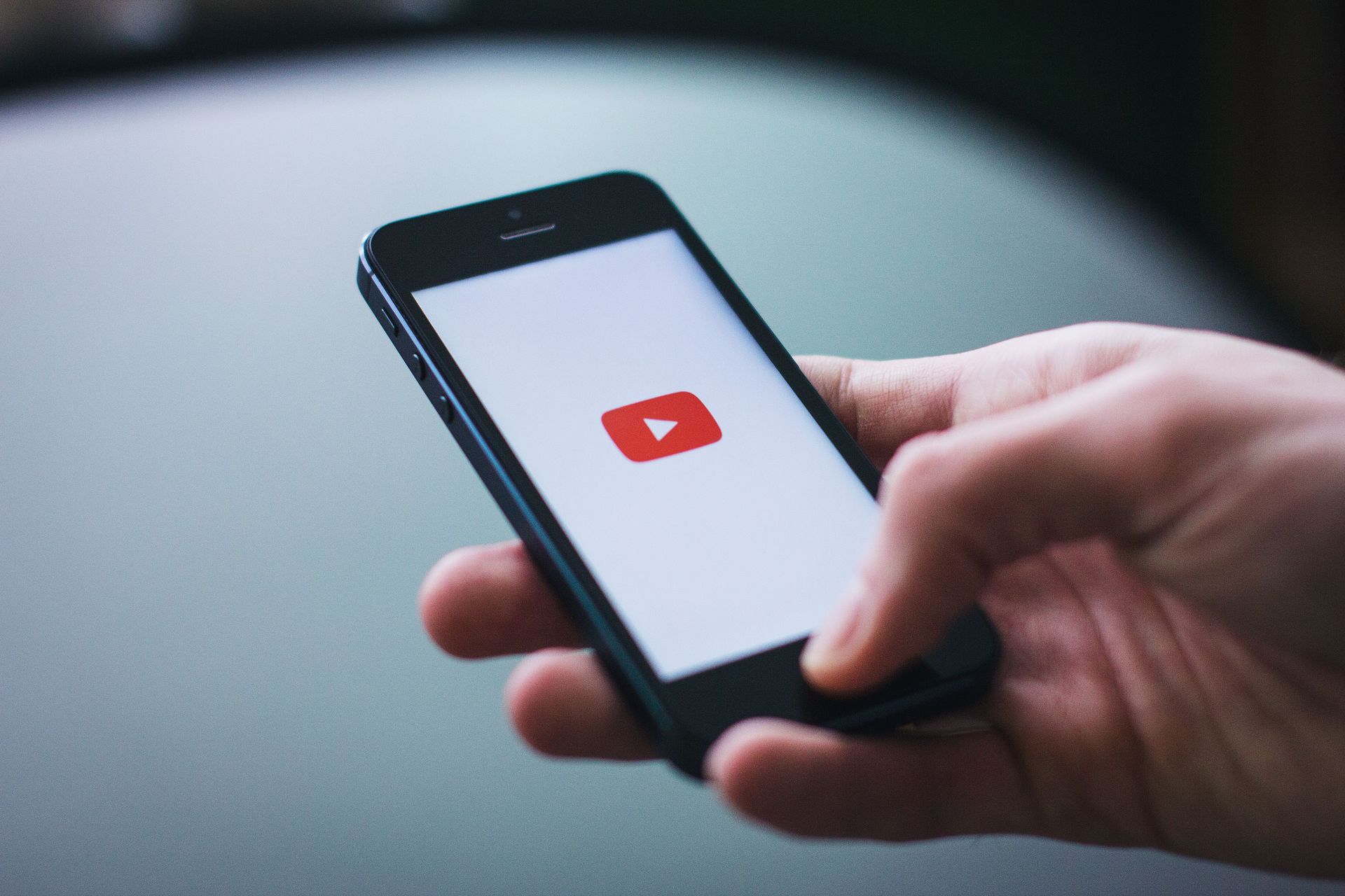 Hand hält ein Smartphone, auf dem das YouTube-Logo auf einem weißen Bildschirm zu sehen ist.