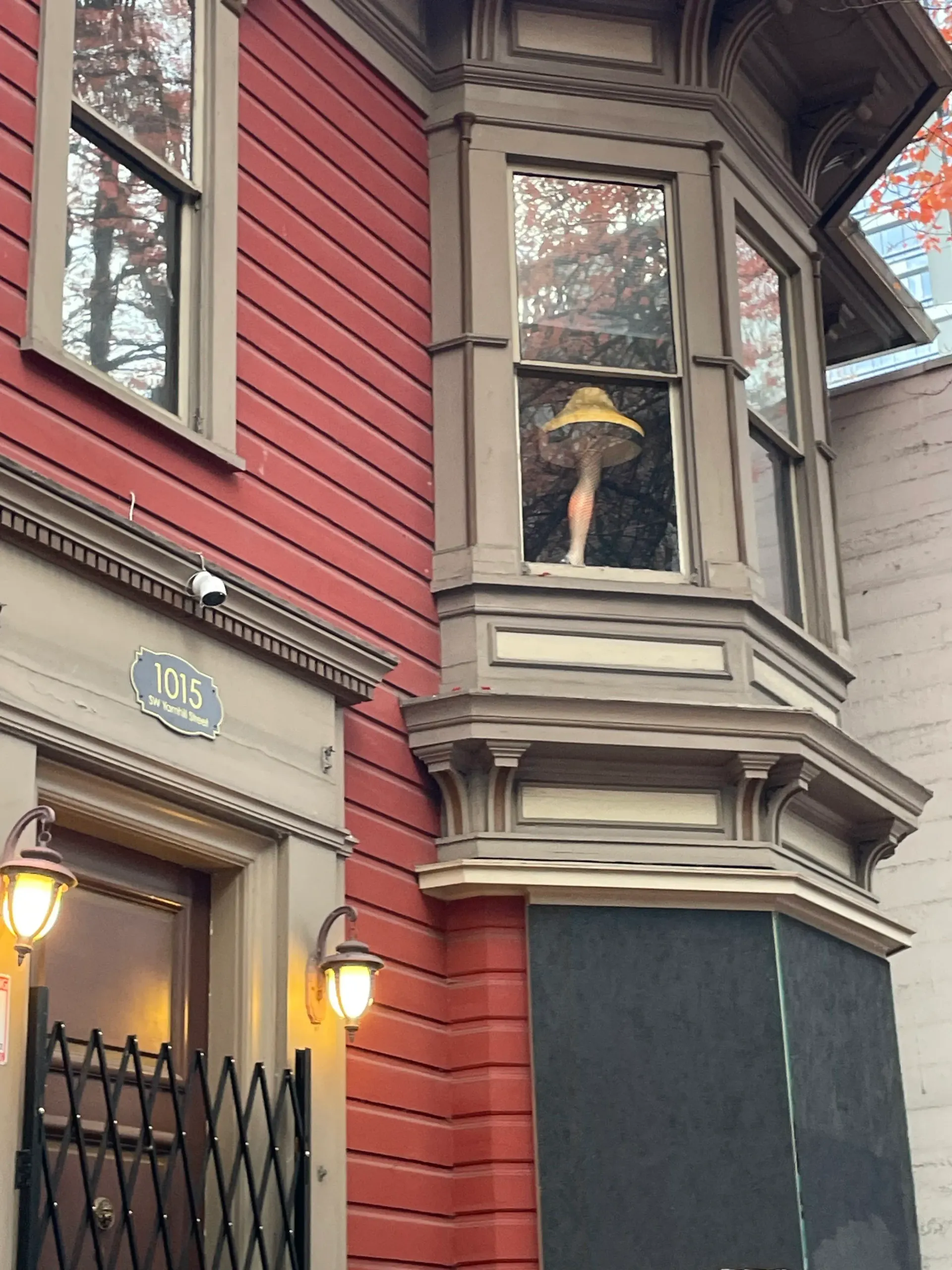 Red building with bay window holding a mannequin leg and lamps. Number 115 above a doorway.