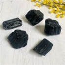 Five rough, black tourmaline crystals on a white surface.