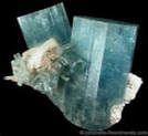 Large, blue-green aquamarine crystal cluster with white matrix against a black background.