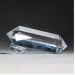 Clear quartz crystal on a small glass base, resting against a dark background.