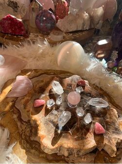Close-up of various crystals on a rustic wooden base, including pink and clear stones with a fluffy white backdrop.