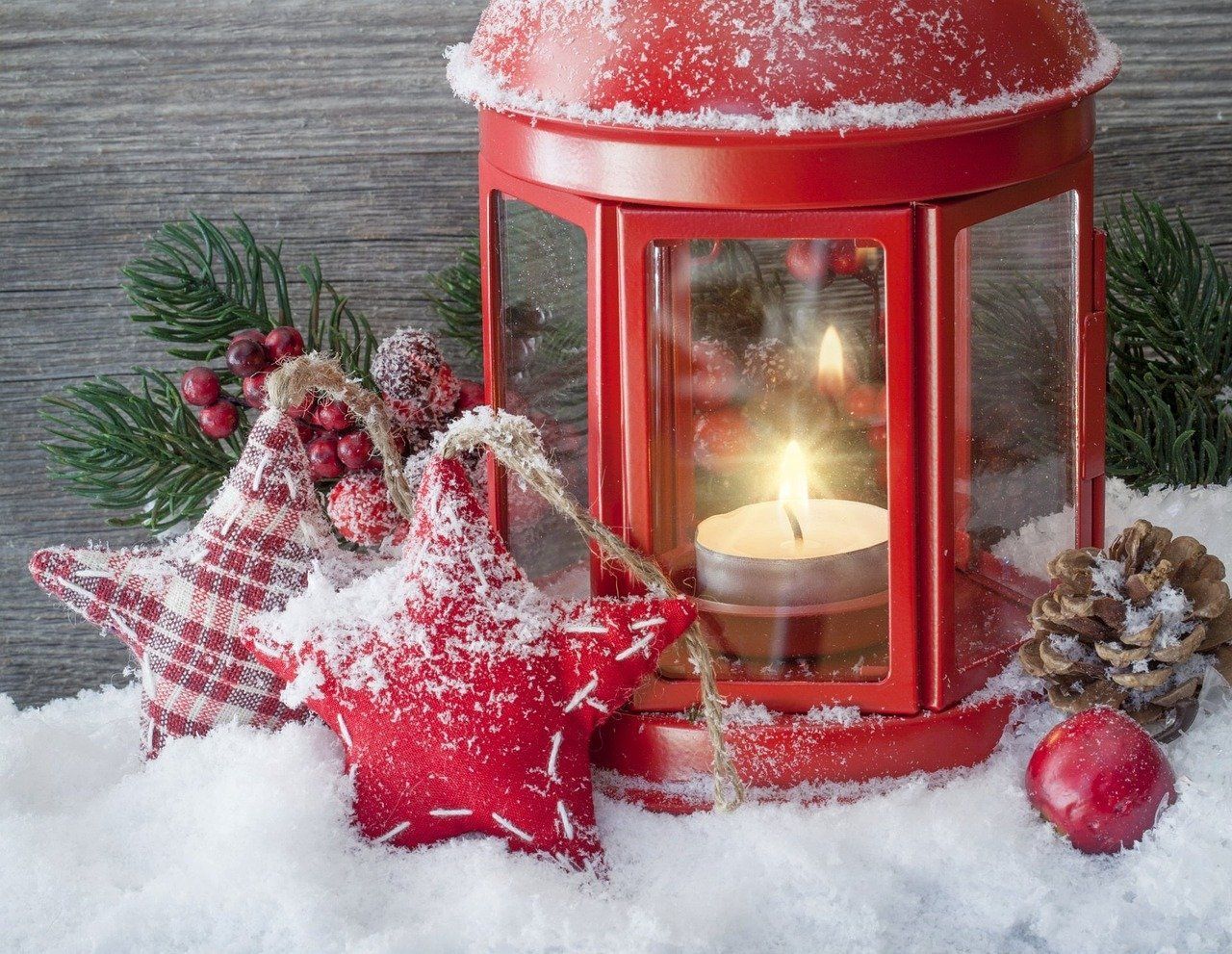 Red lantern with lit candle, star ornaments, pine, and berries in snow.