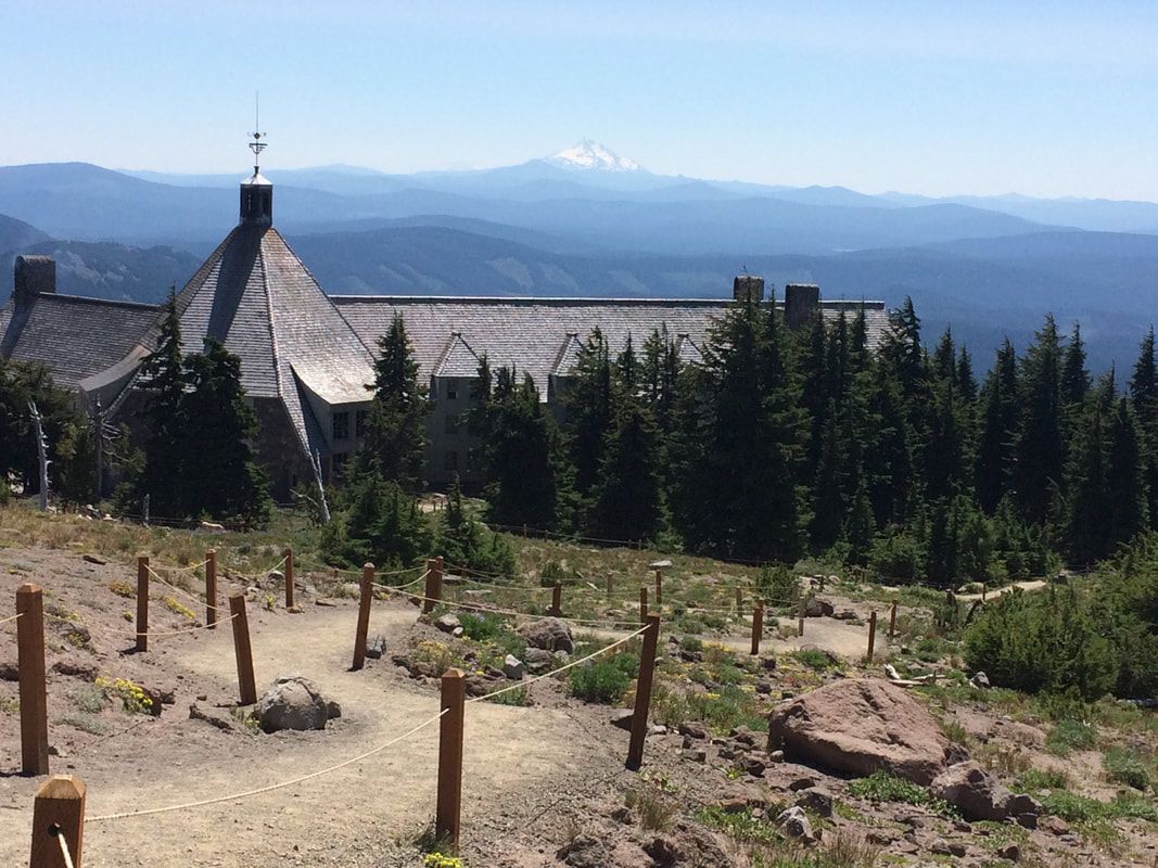 Stone lodge on a hillside trail, forested with a snowy mountain in the distance.