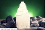 White selenite tower surrounded by gray and black rocks with green backdrop.