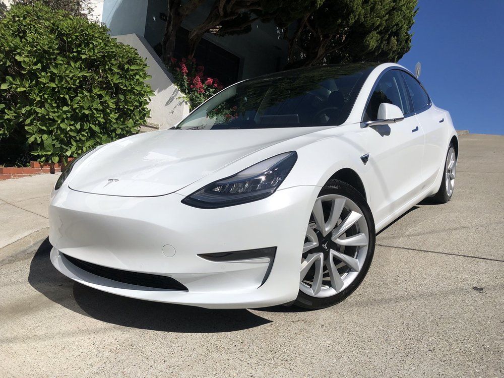 A white tesla model 3 is parked on the side of the road.
