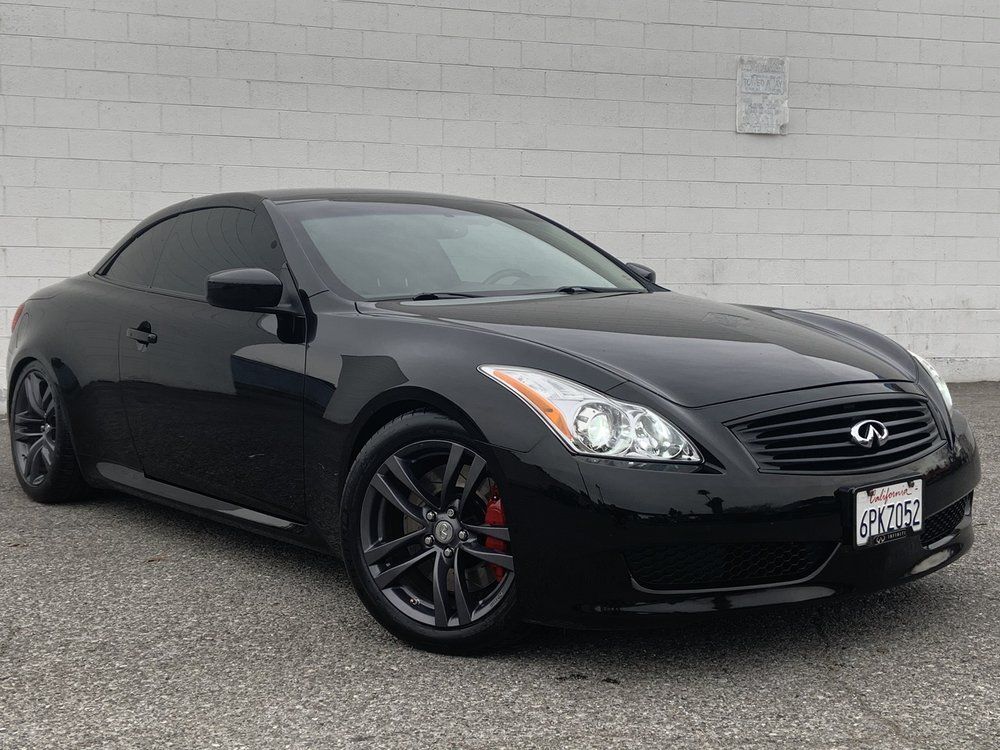 A black sports car is parked in front of a white brick building.