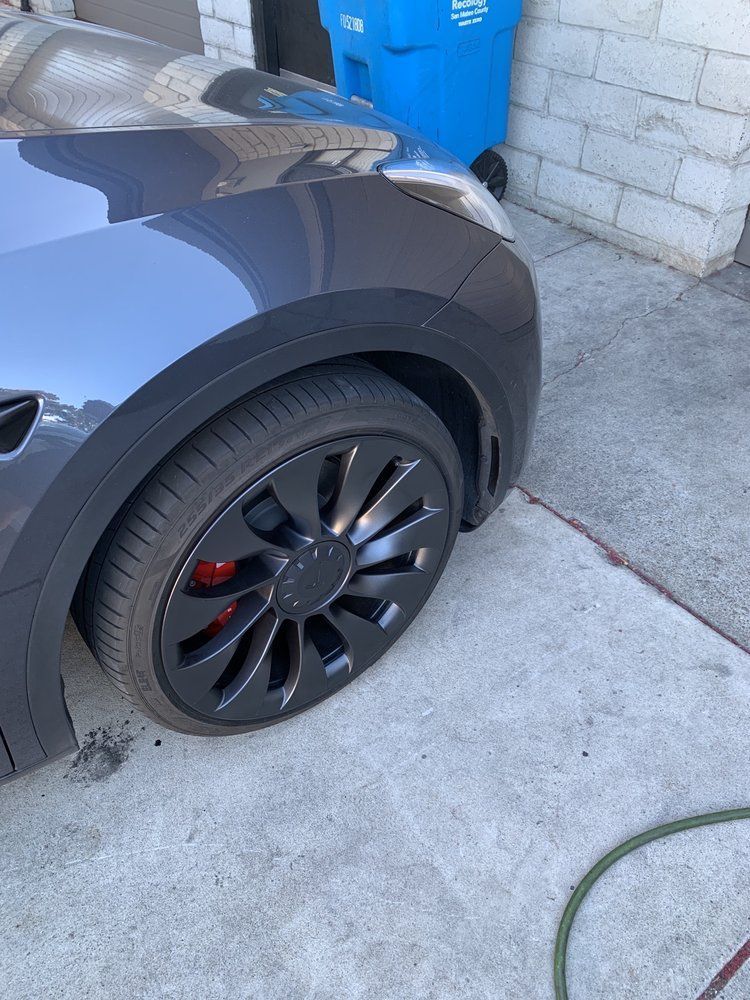 A tesla model 3 is parked in a driveway next to a blue trash can.