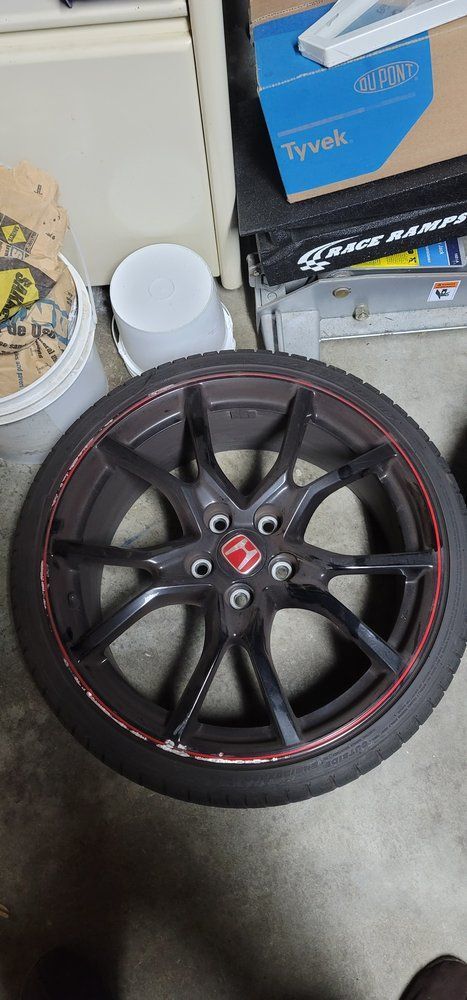 A black wheel with a red rim is sitting on a concrete floor.