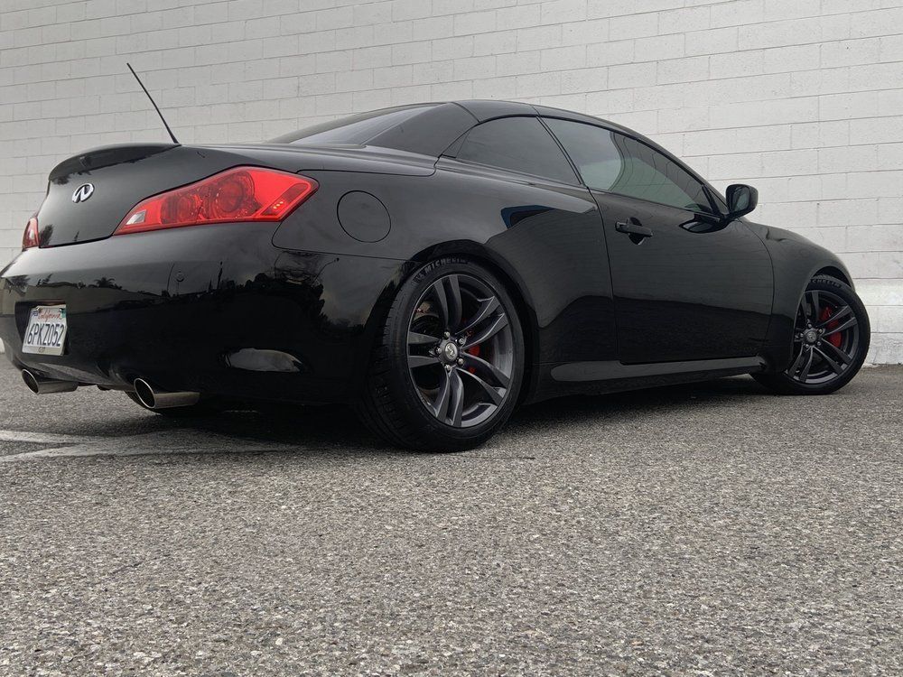 A black sports car is parked in a parking lot in front of a white brick building.