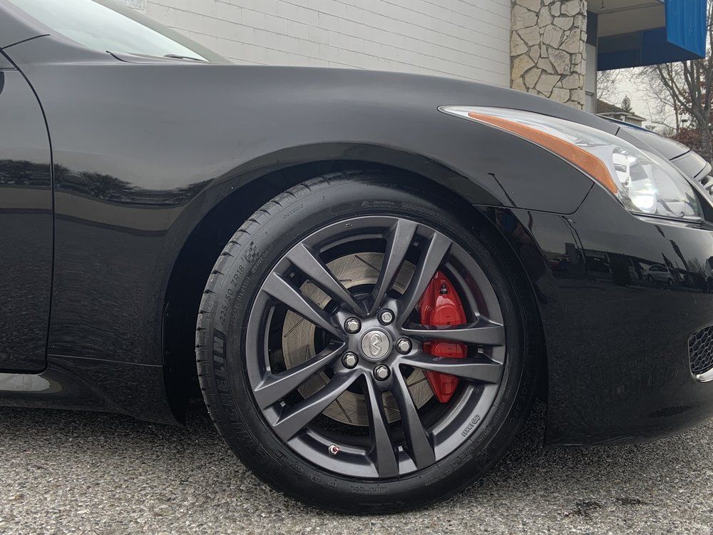A black car with red brake calipers is parked in front of a building
