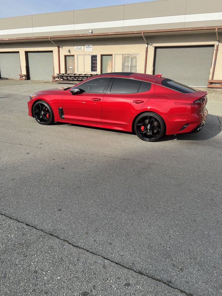 A red car is parked on the side of the road in front of a building.