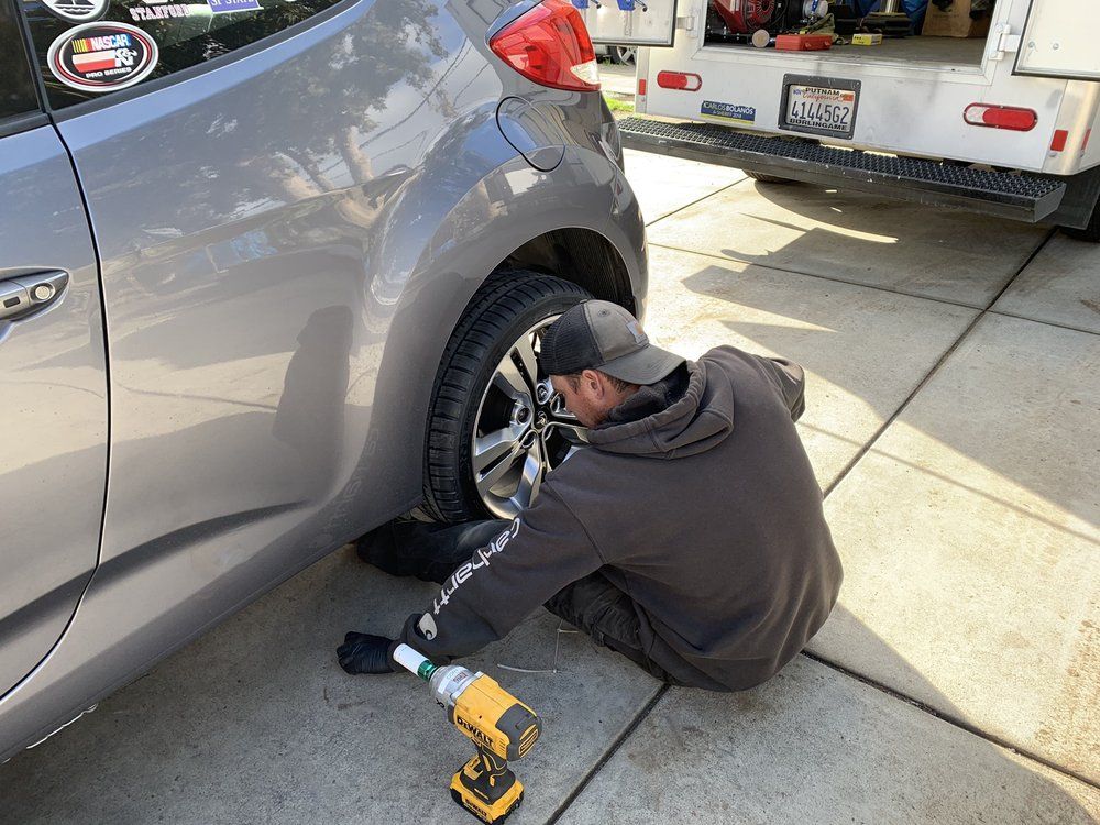 A man is kneeling down to change a tire on a car.