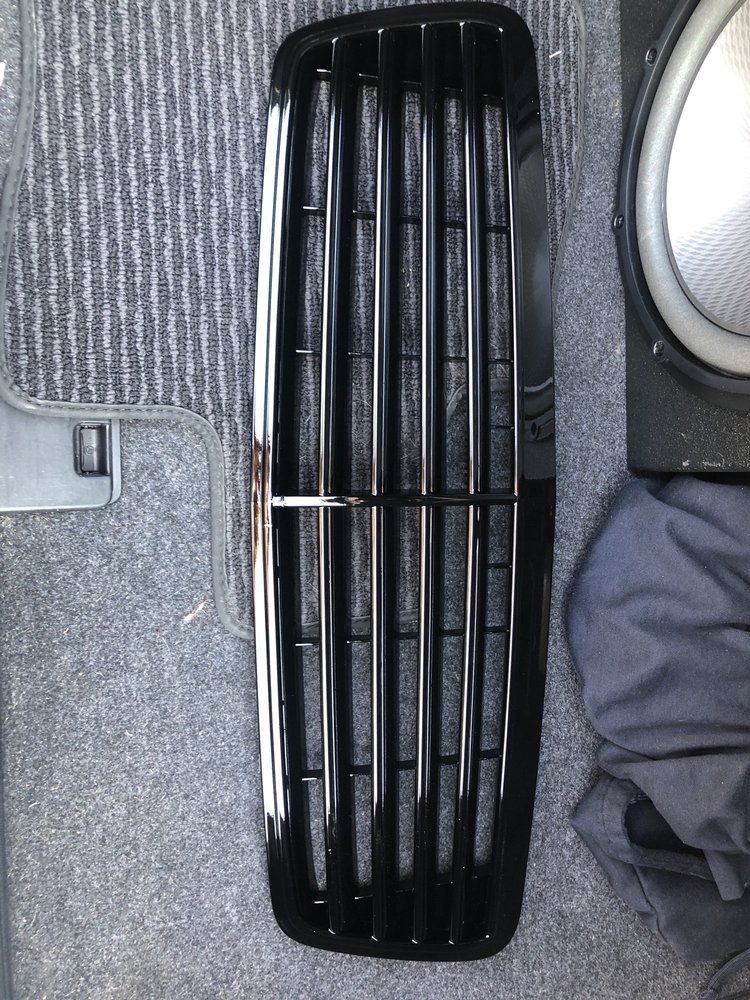 A black grill sits on a carpet next to a speaker