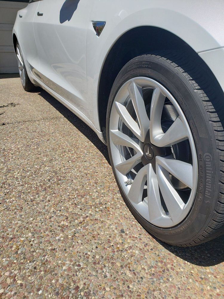 A white tesla model 3 is parked on a gravel driveway.