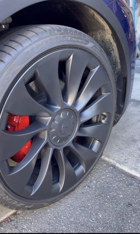 A close up of a tesla model 3 wheel with red brake calipers.