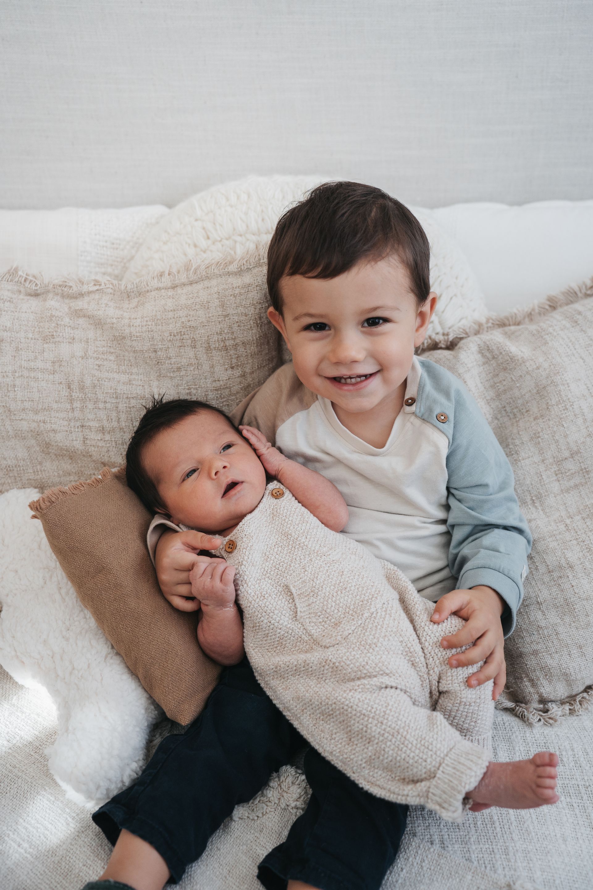 Ein kleiner Junge hält ein neugeborenes Baby auf einem Sofa.