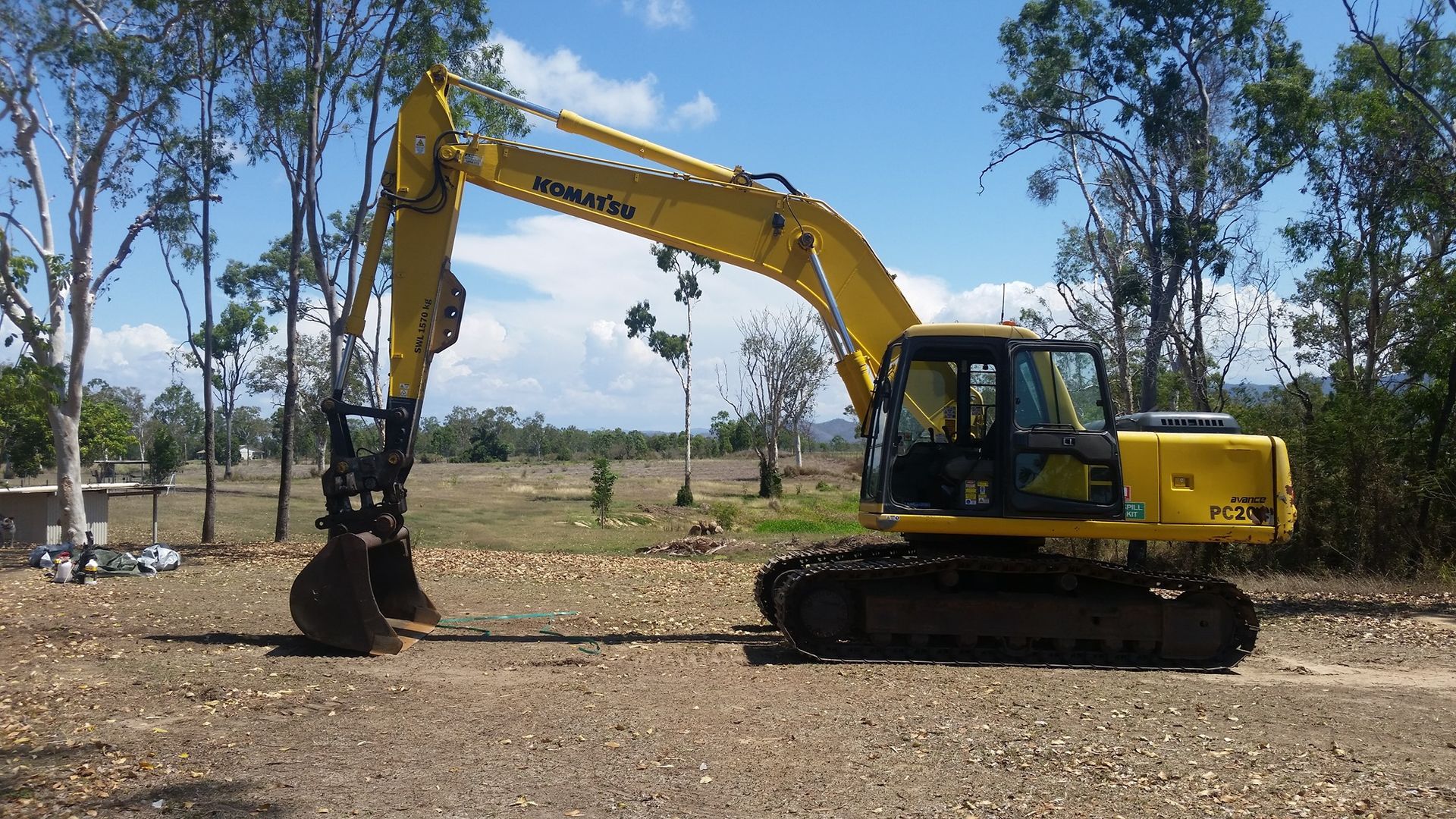 A Yellow Excavator Is Parked In A Dirt Field With Trees In The Background — Allsites Earthworx In Garbutt, QLD