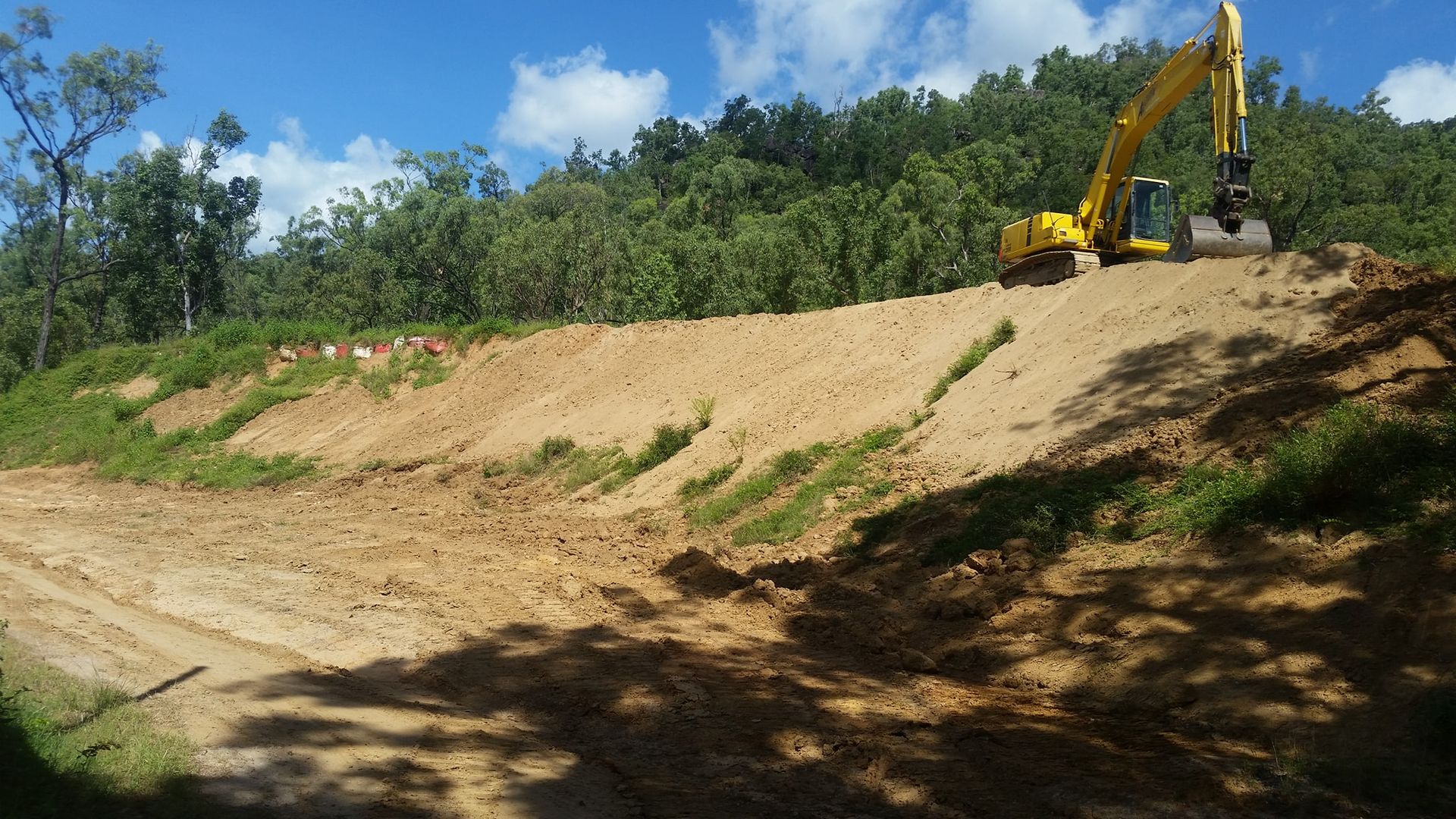 A Yellow Excavator Is Working On A Dirt Hill — Allsites Earthworx In Garbutt, QLD