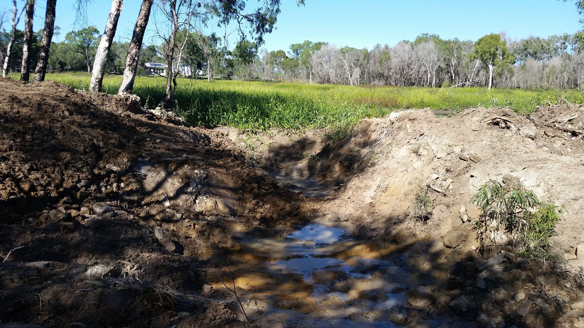 A Muddy Stream Running Through A Field With Trees In The Background — Allsites Earthworx In Garbutt, QLD