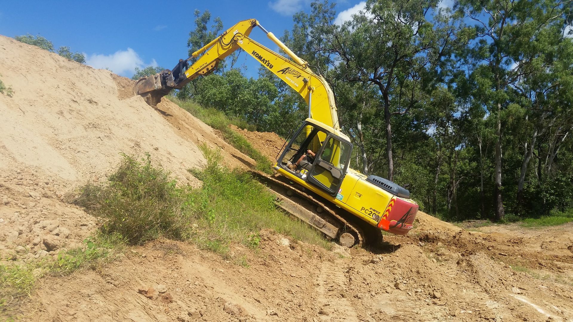 A Yellow Excavator Is Driving Down A Dirt Hill — Allsites Earthworx In Garbutt, QLD