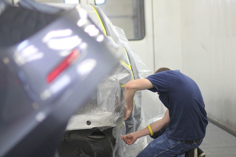 auto body technician at crossroads collision, inc., taping off car for painting process