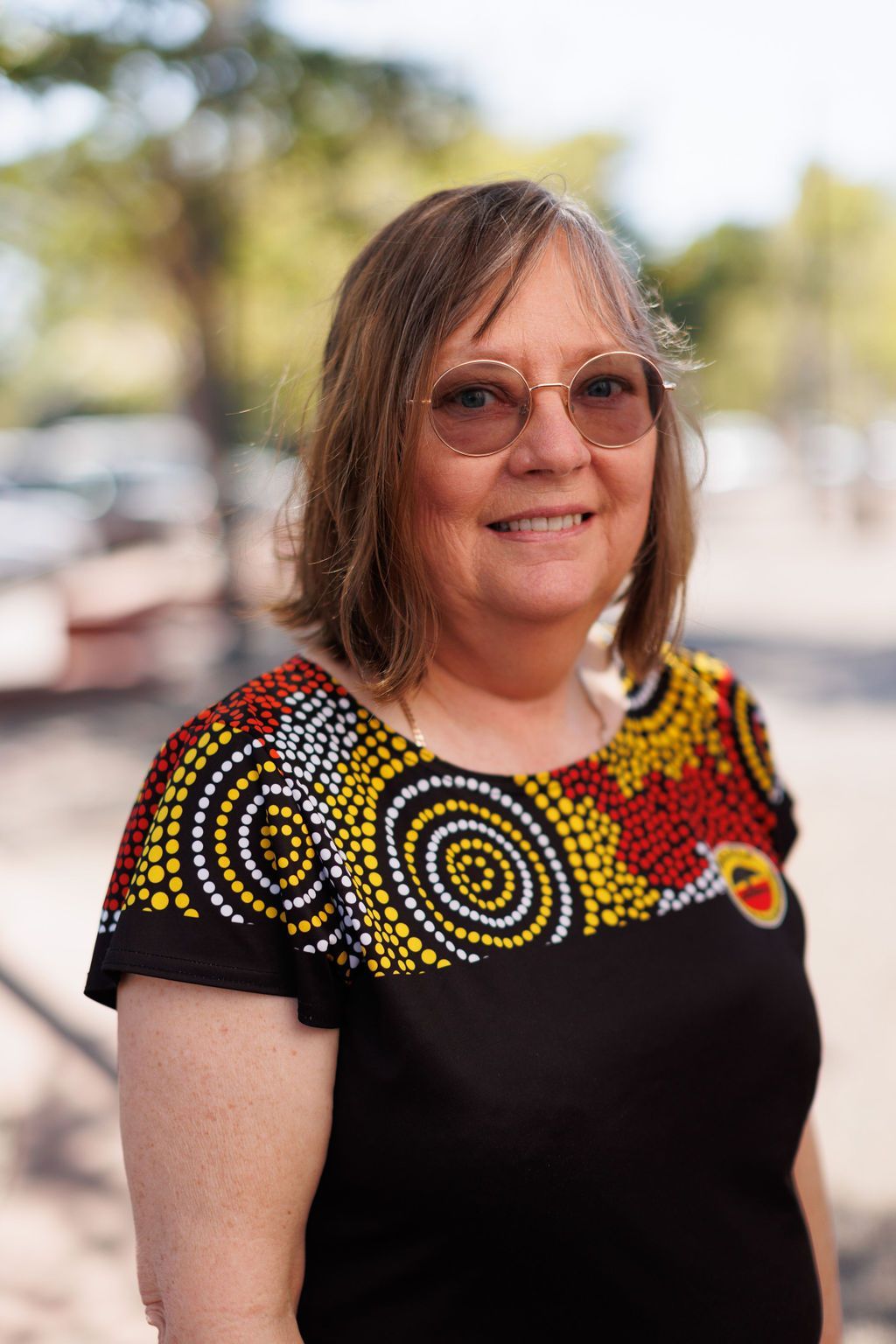 A woman wearing glasses and a black shirt is standing in front of a tree.