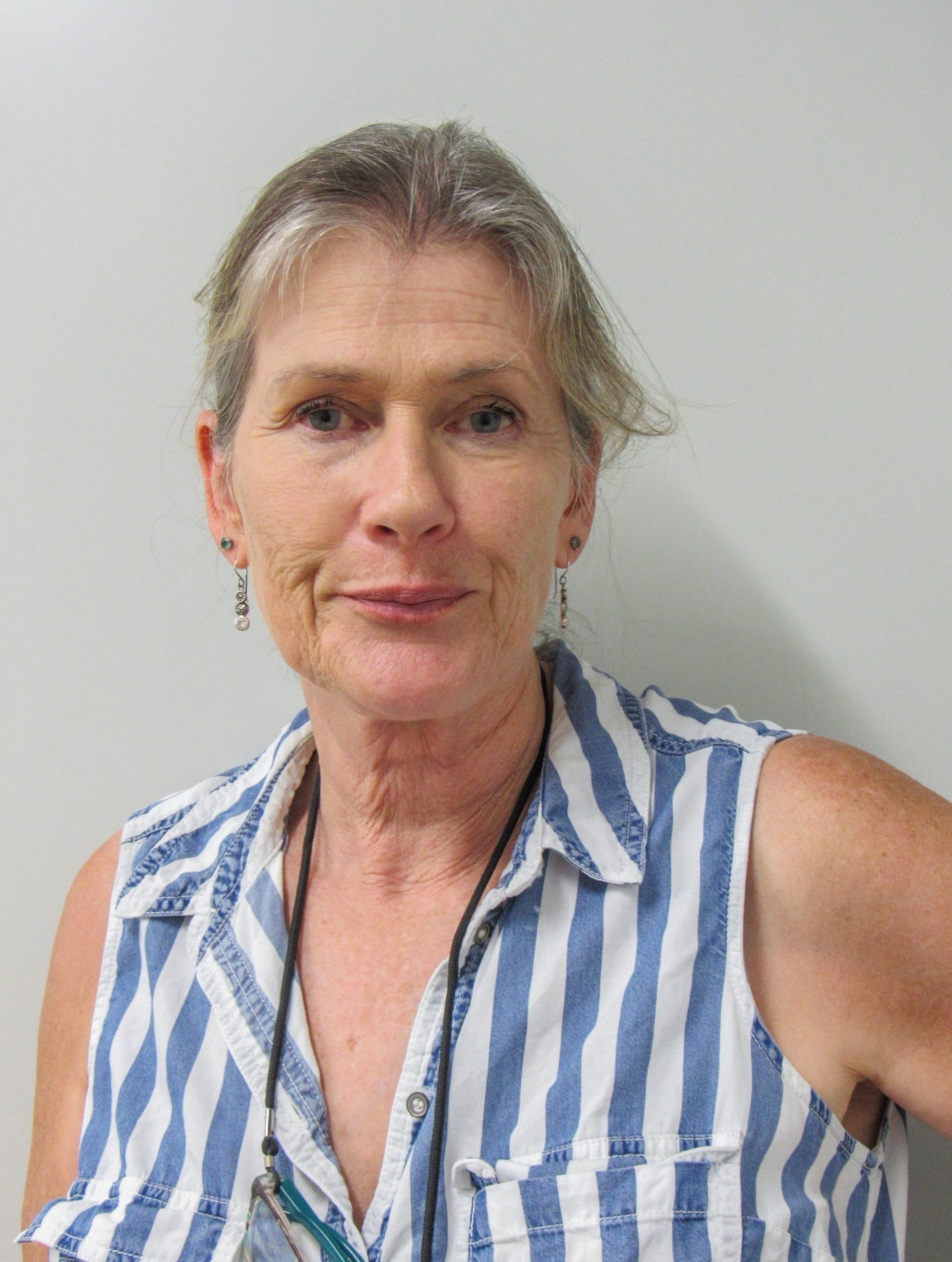A woman wearing a blue and white striped shirt is standing in front of a white wall.