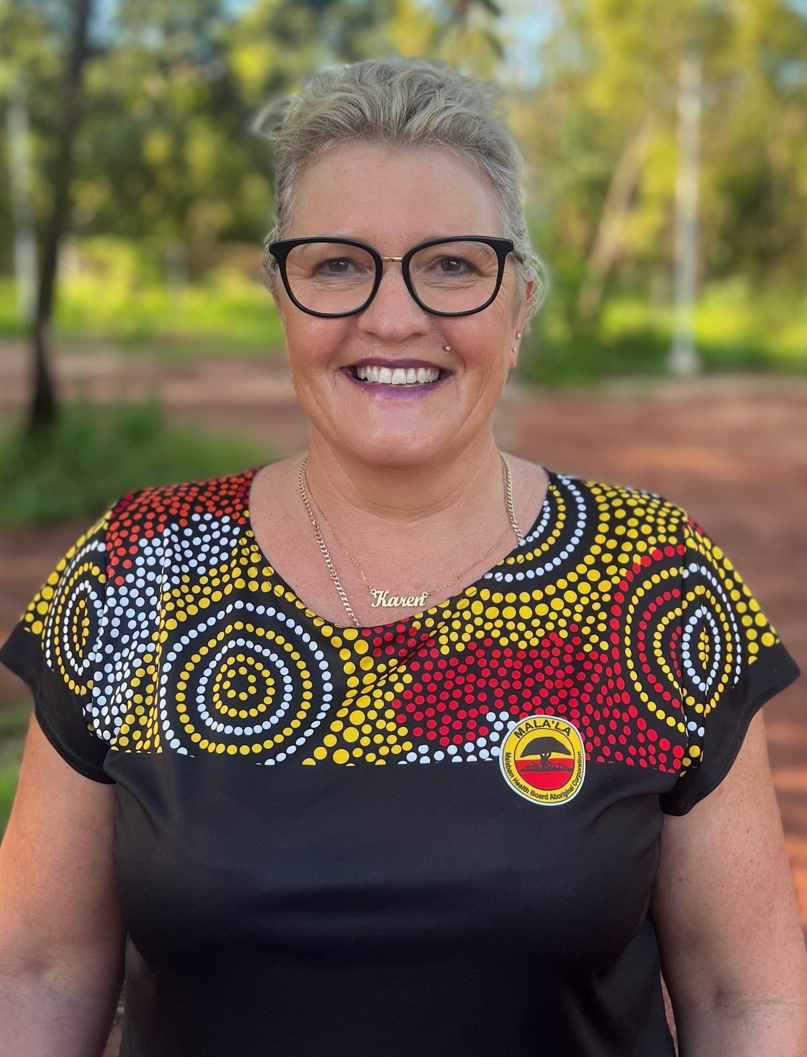 A woman wearing glasses and a colorful shirt is smiling for the camera.
