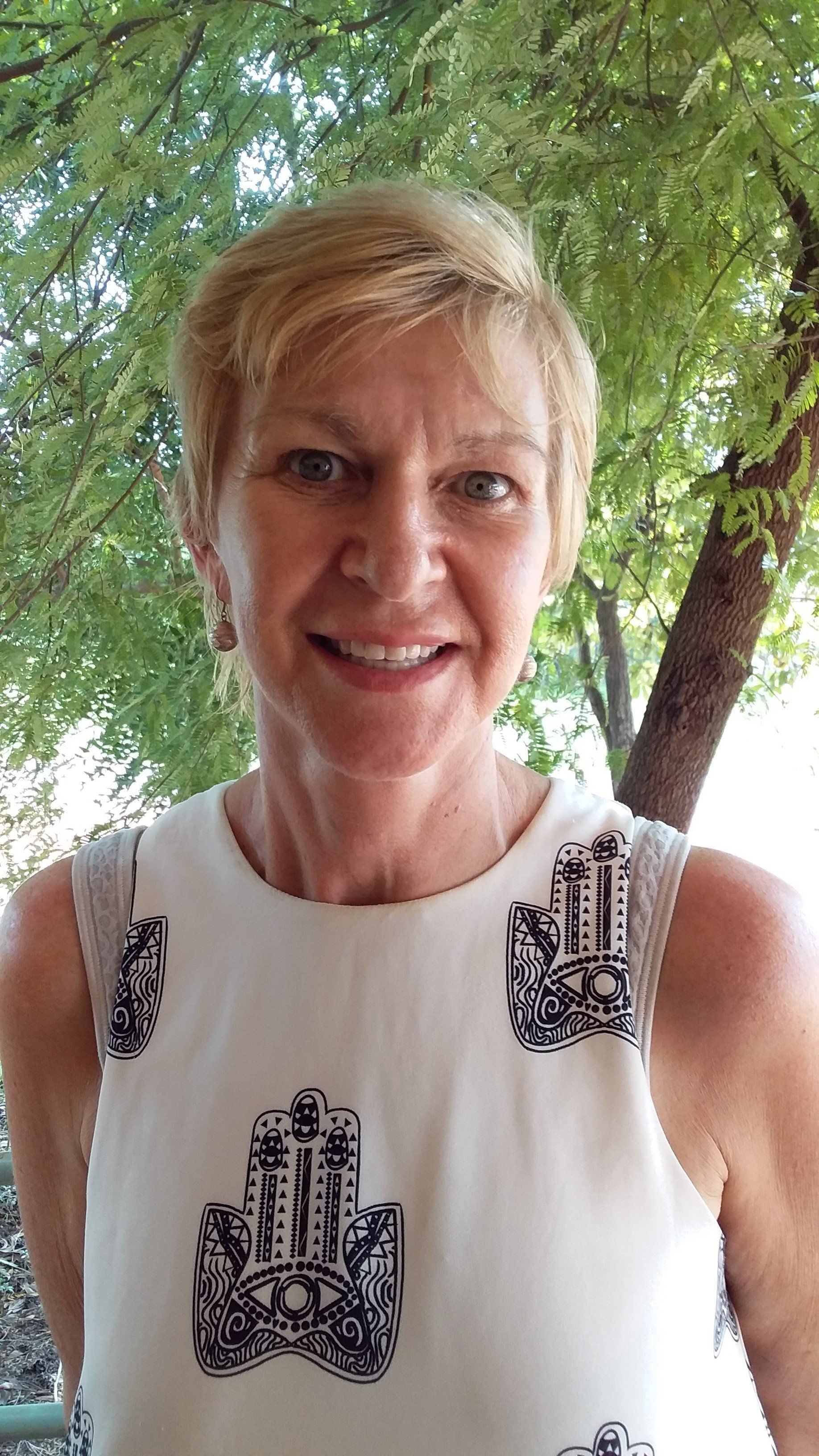 A woman in a white dress is smiling in front of a tree.