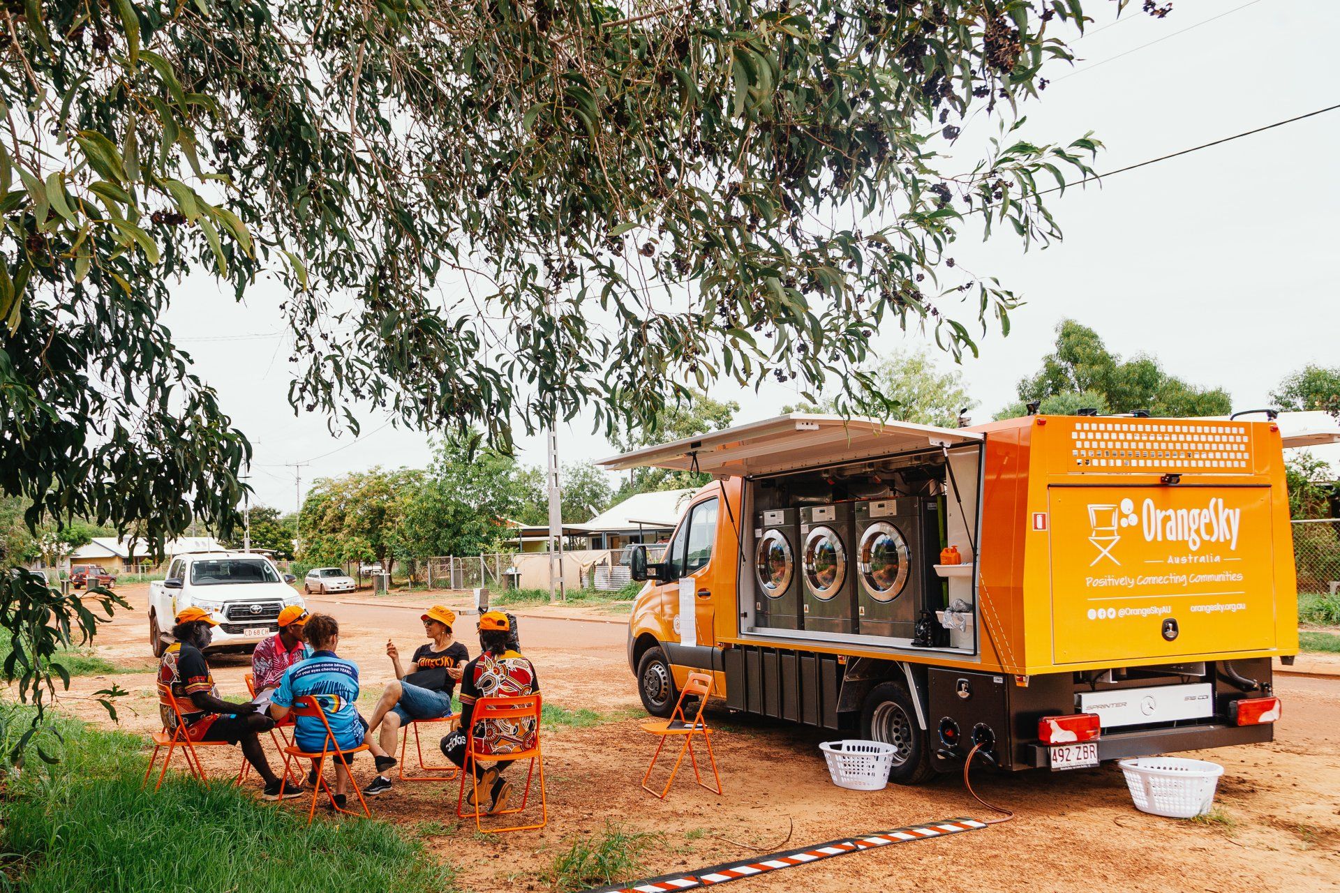 A group of people are sitting around a table in front of a laundromat truck.