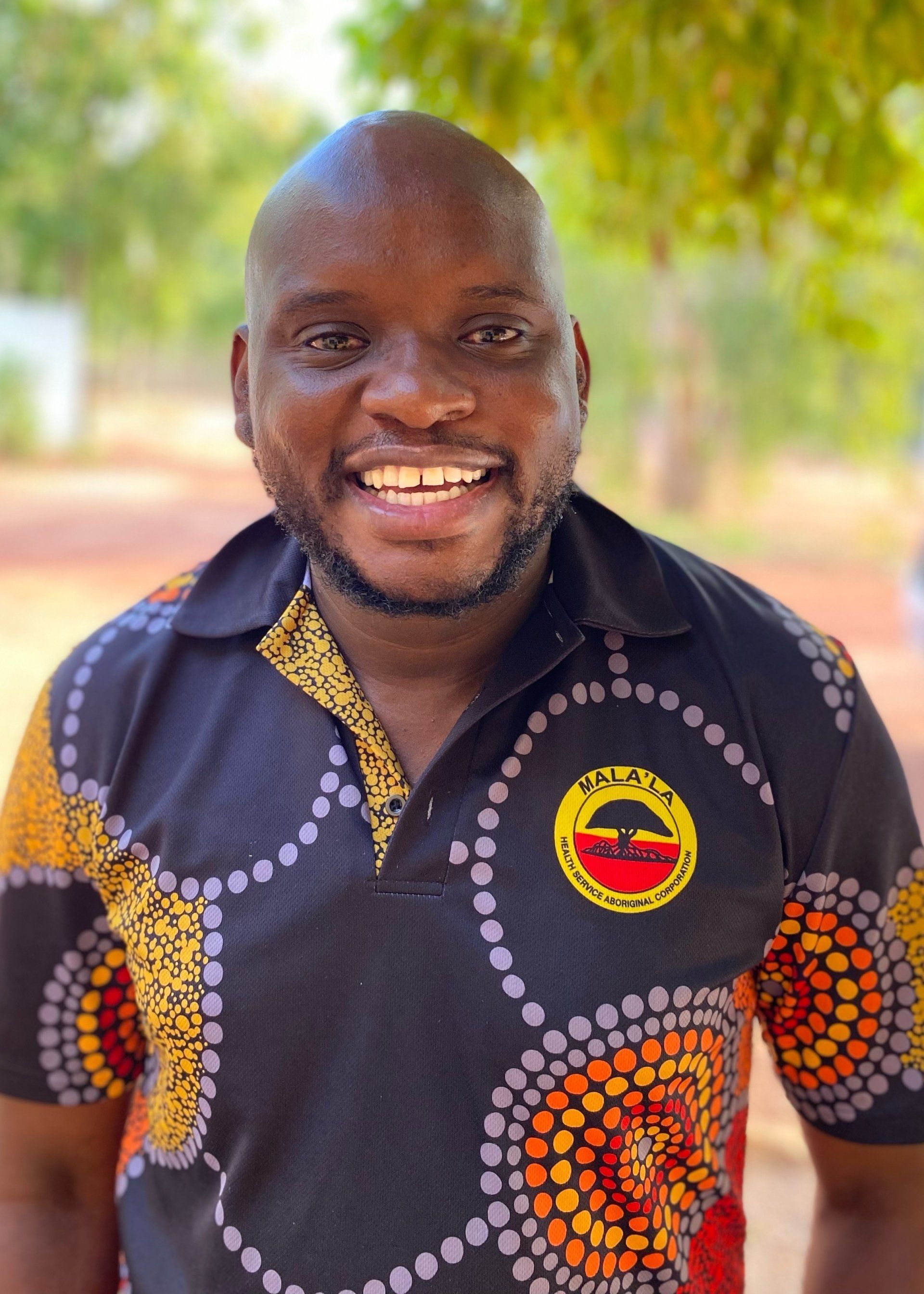 A bald man with a beard is wearing a black and orange shirt and smiling.