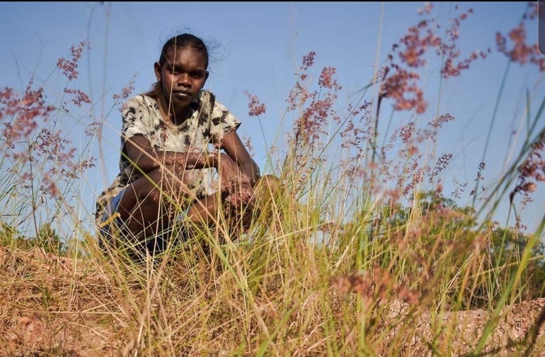 A young girl is kneeling in a field of tall grass.