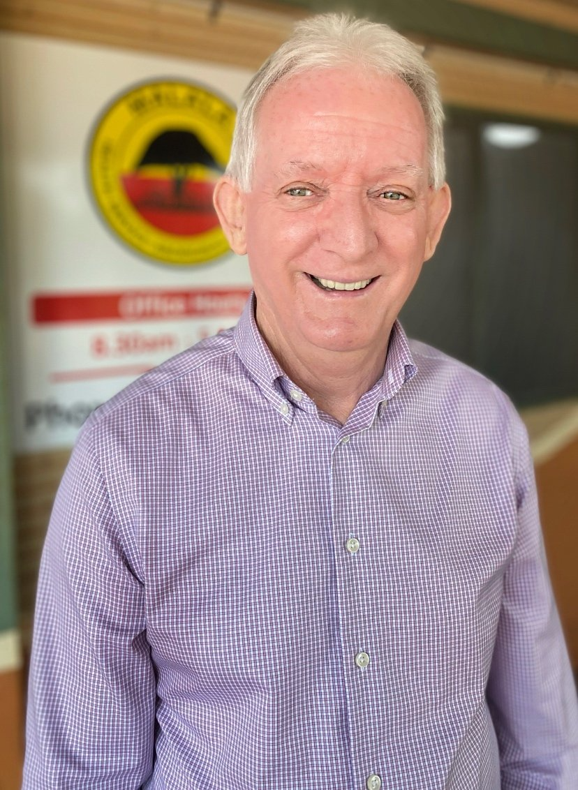 A man in a purple shirt is smiling in front of a sign.