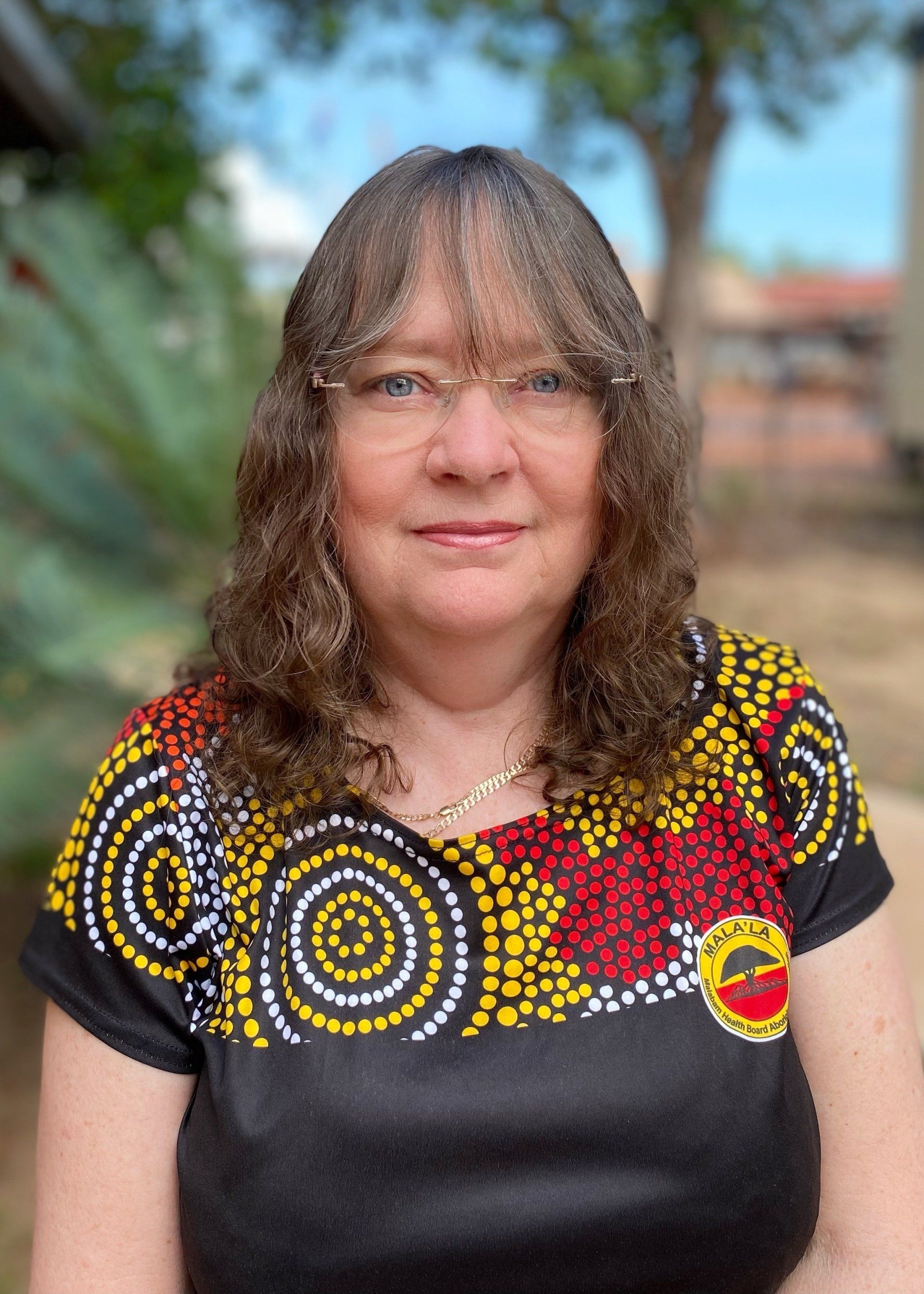 A woman wearing glasses and a black shirt is standing in front of a tree.