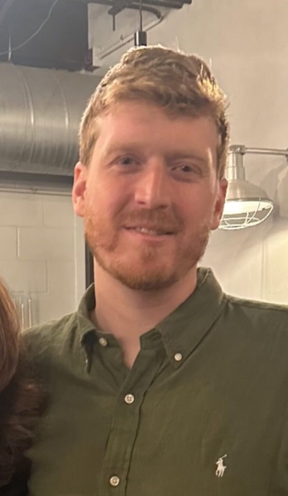 Man with reddish-blond hair and beard, wearing a green button-down shirt, smiling.
