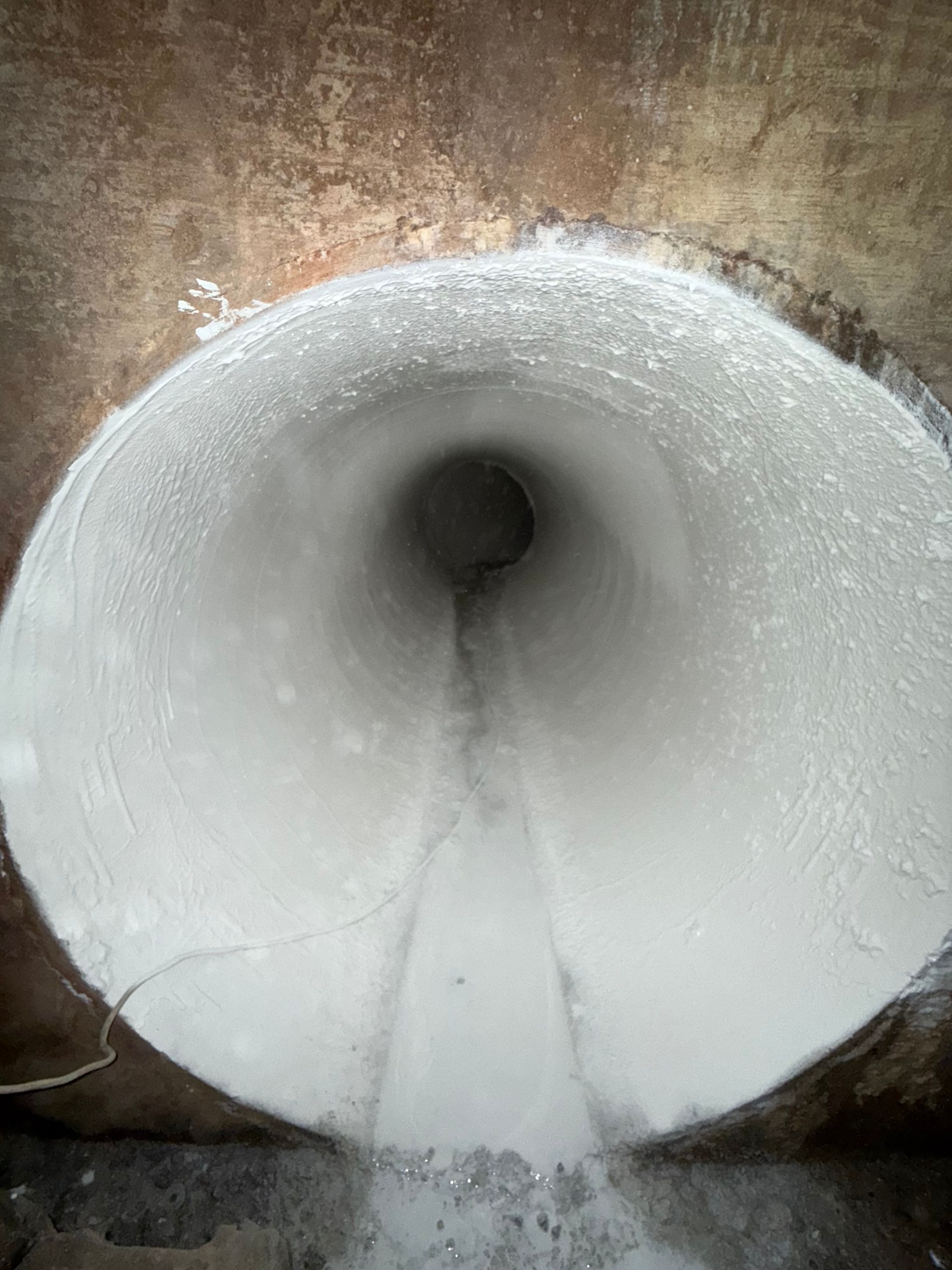 View down a concrete tunnel with white coating, water flowing.
