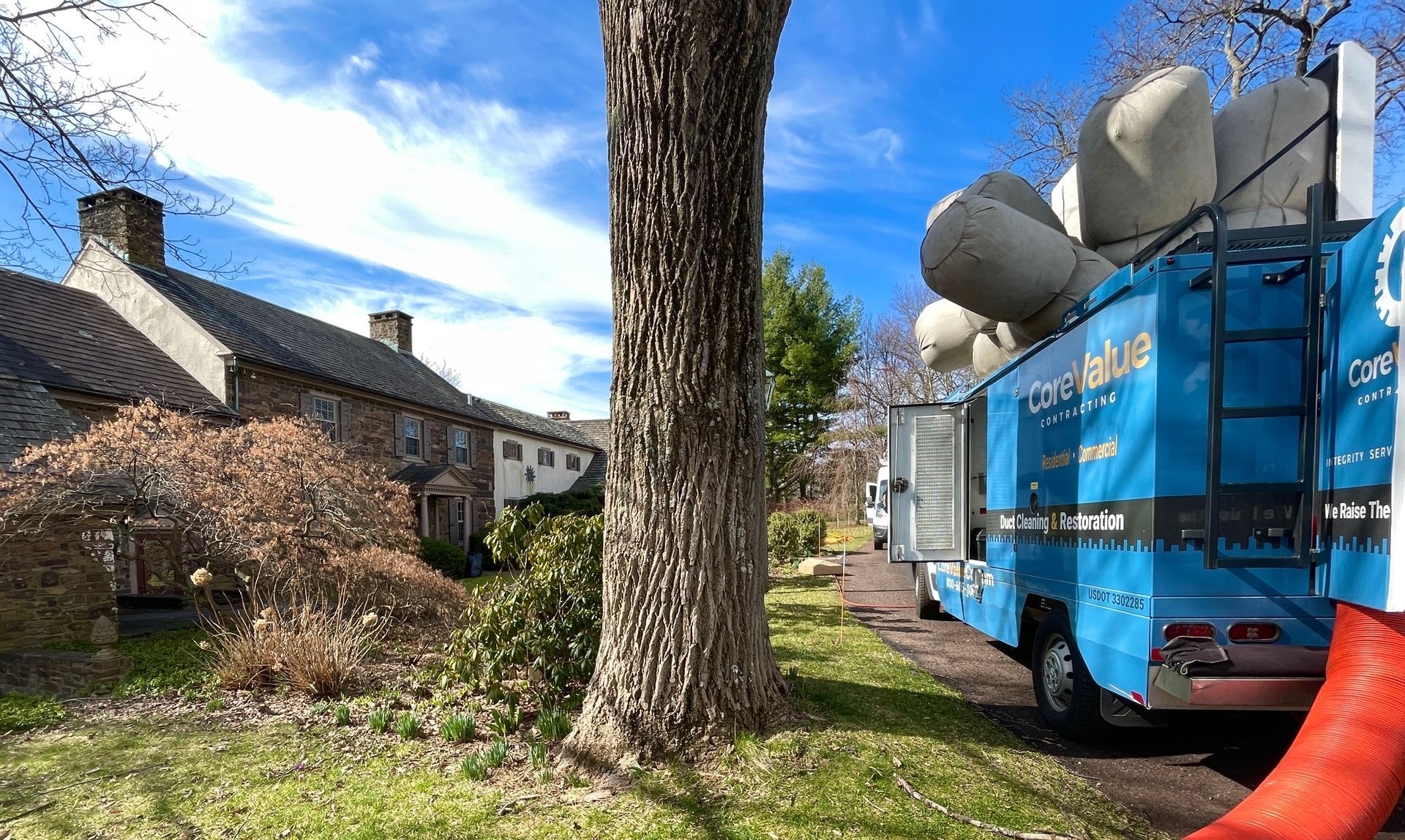 Blue moving truck parked on a road beside a historic stone building and tree, carrying large bundles.