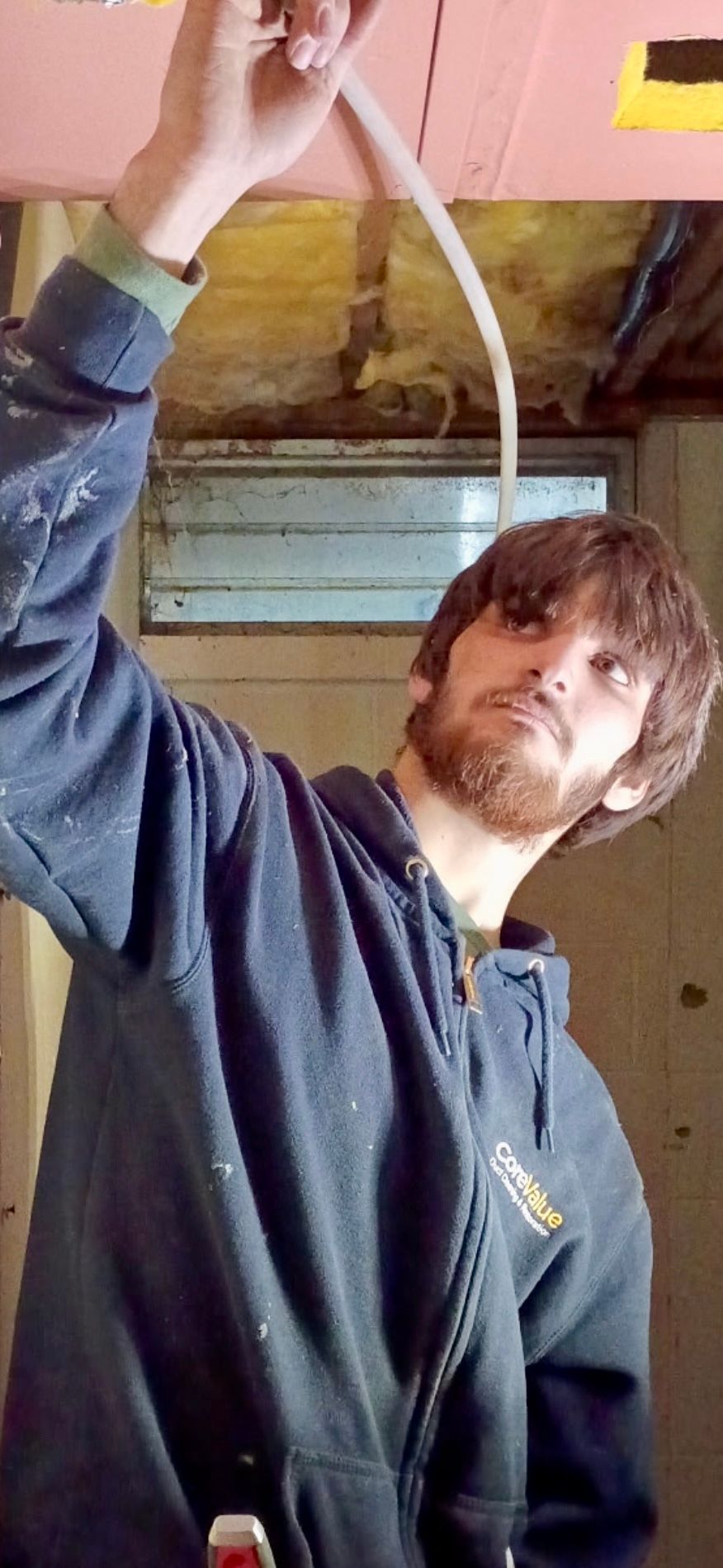 Man in cap repairs a wall-mounted air conditioner in a room with a window and white walls.