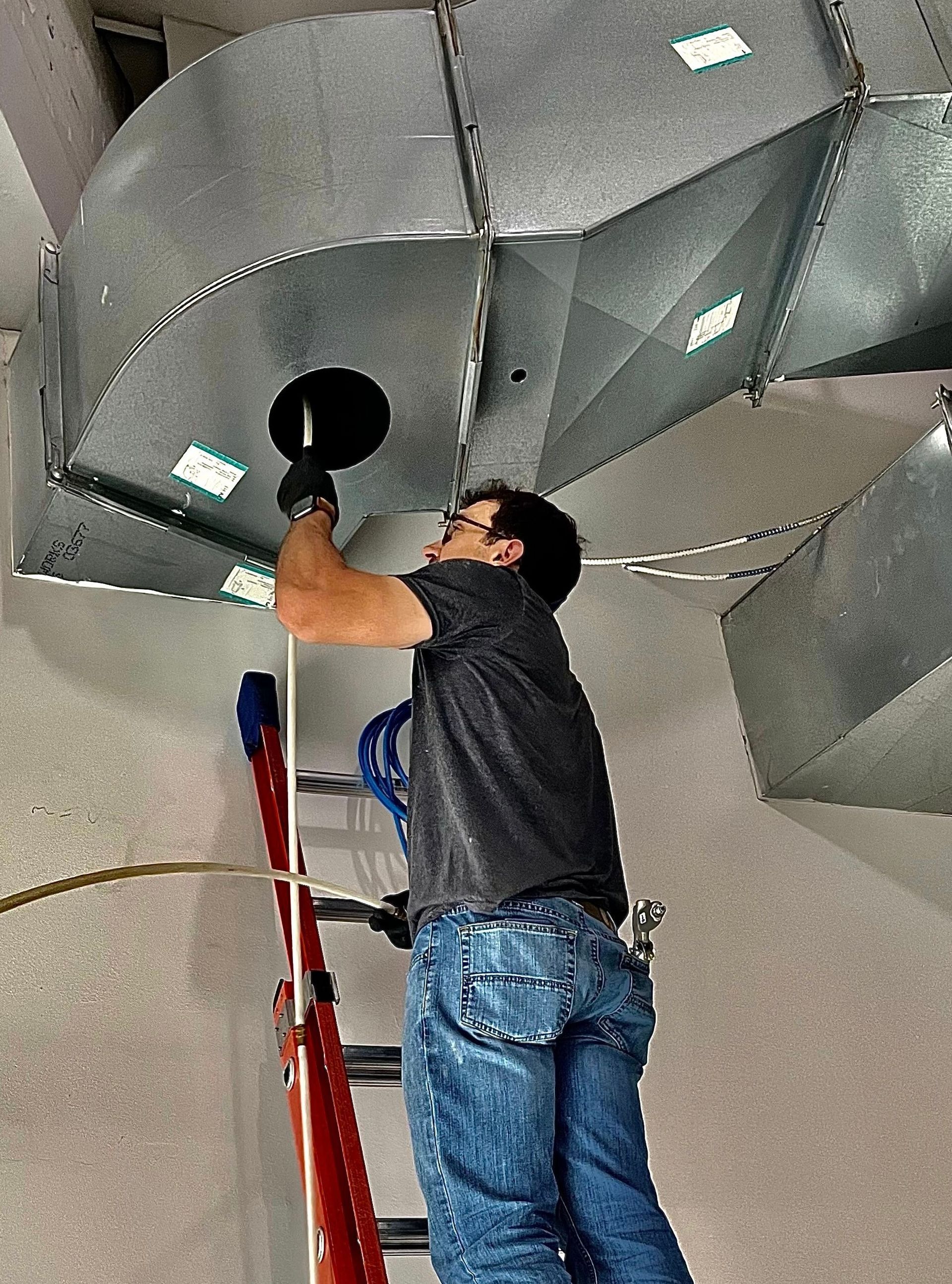 Person on ladder installing ventilation ductwork.