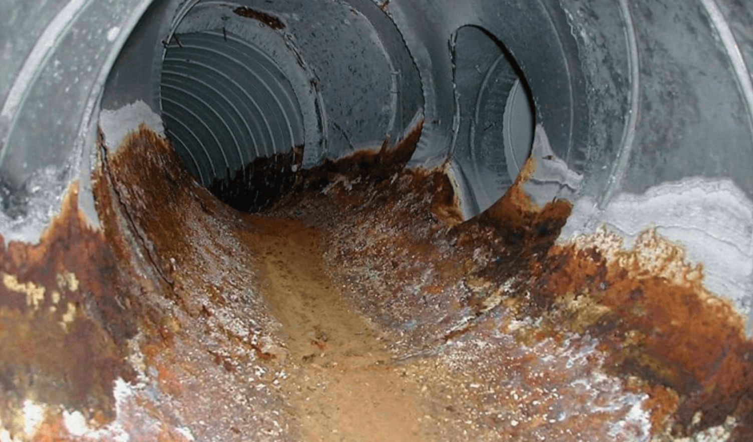 Severely corroded metal ductwork with rust and debris inside.