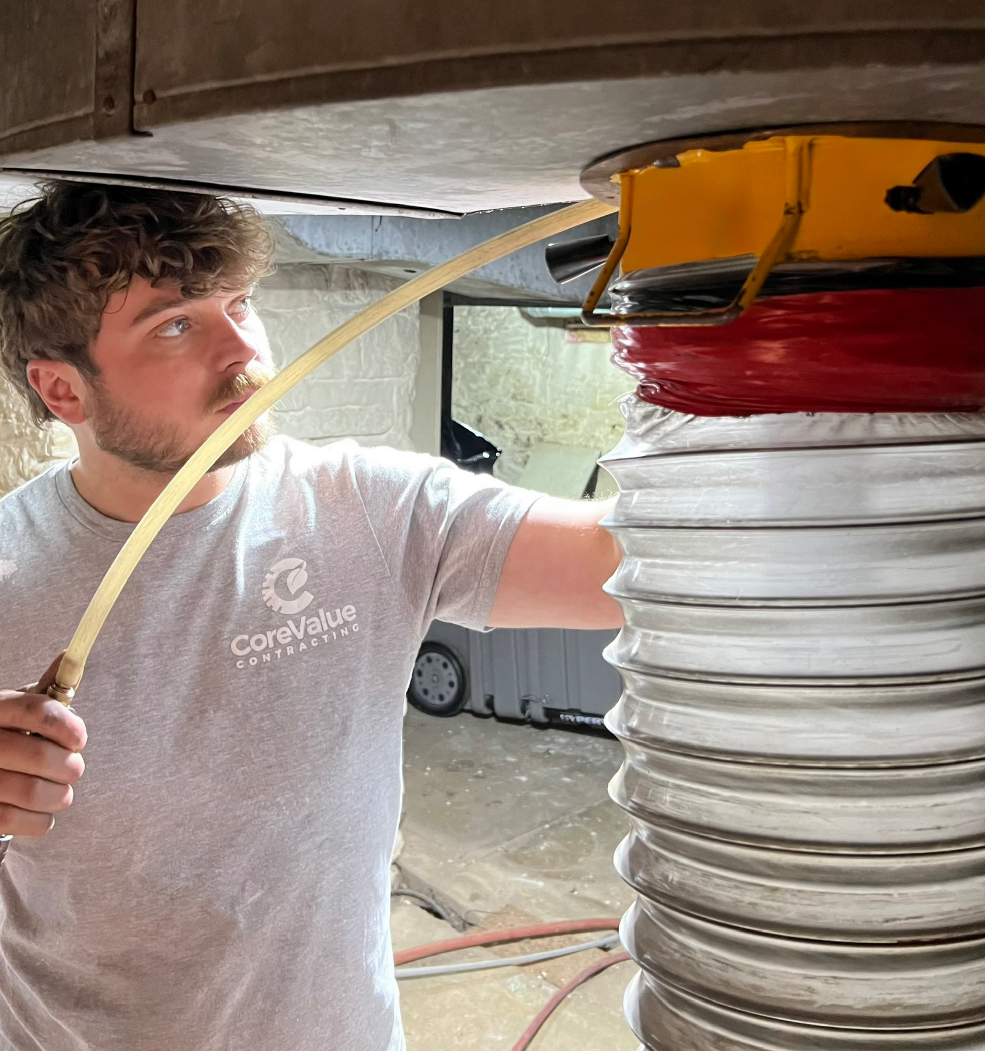 Man working on equipment, holding a tube. Equipment is metal, red, and yellow. Indoor setting.