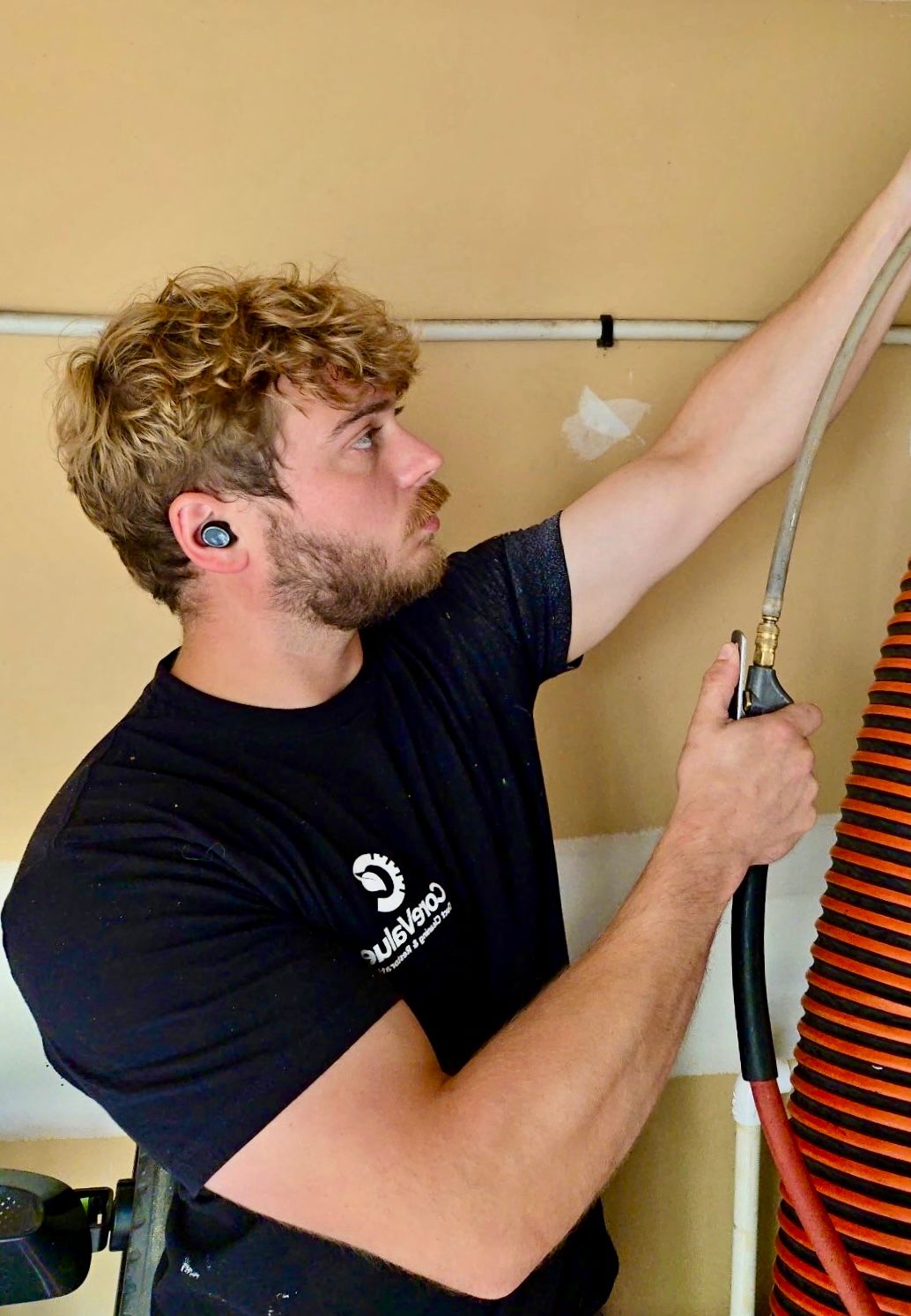 Man in black shirt with earbuds, holding a hose, looking up.