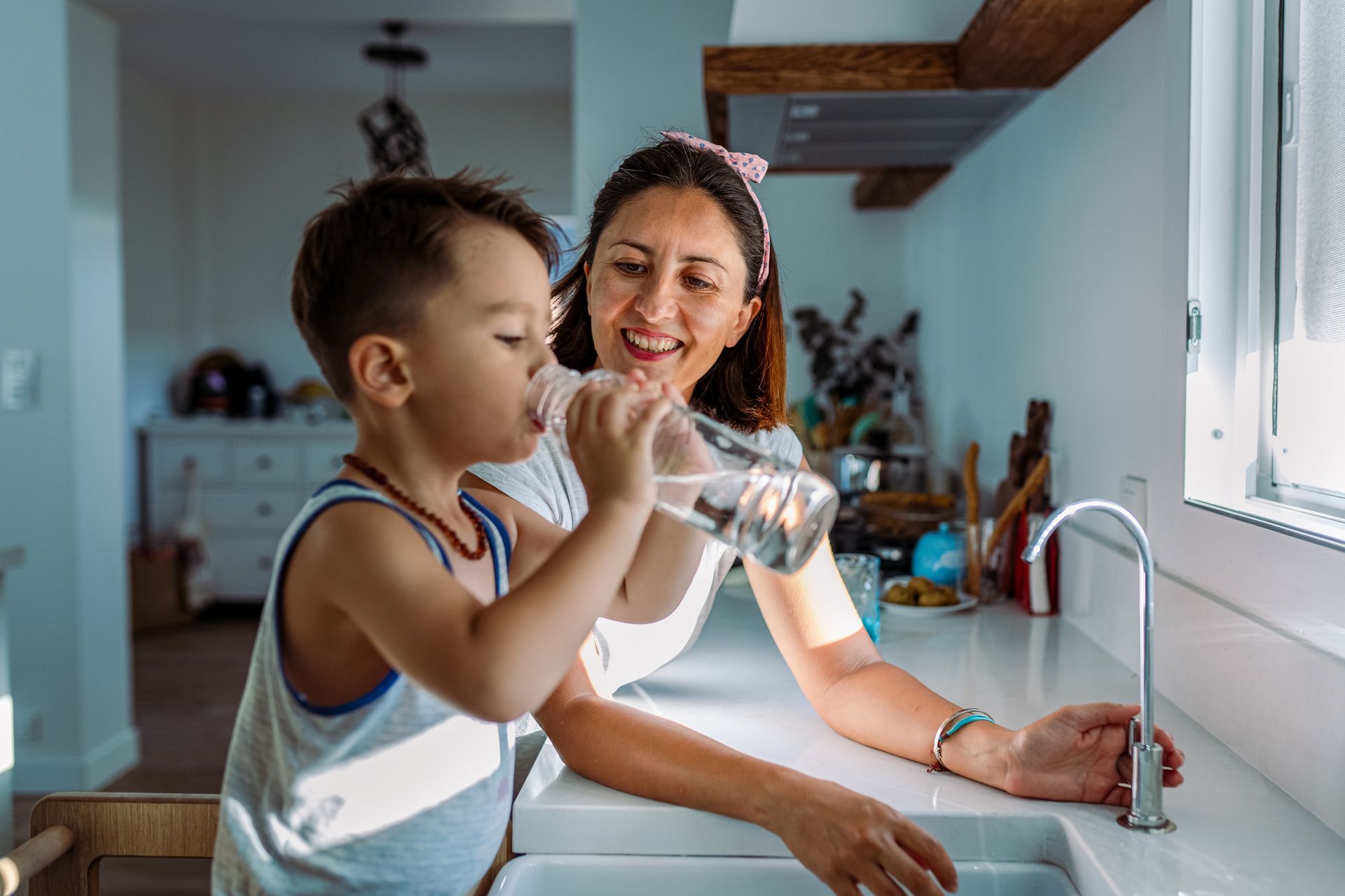 Mother smiling as her son drinks clean water from faucet with well water filtration system.